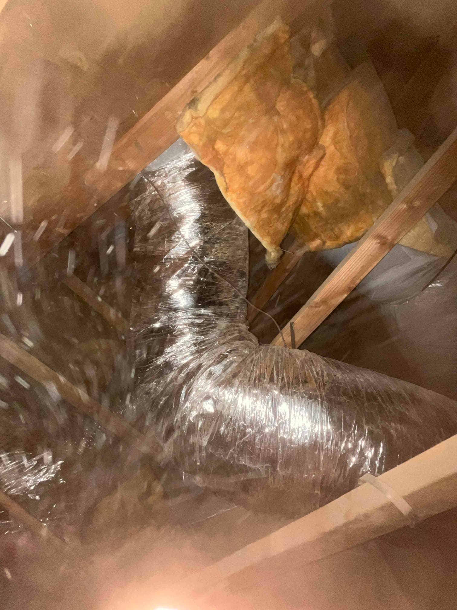 Flexible insulated ductwork routed through the attic, secured between framing members with fiberglass batt insulation nearby.