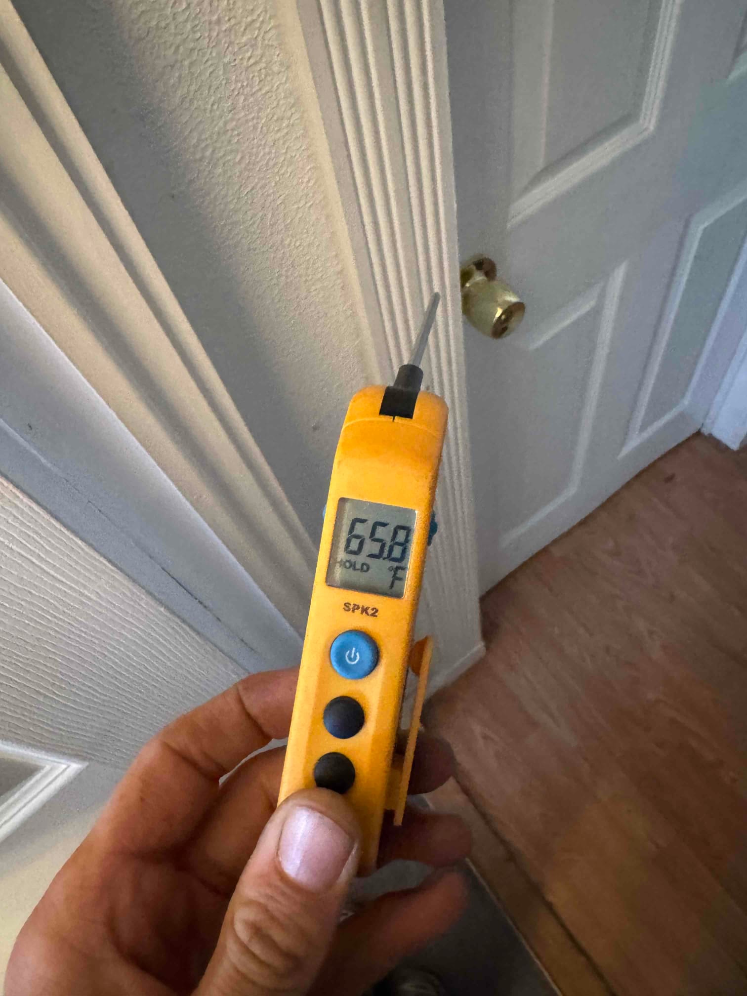 Handheld digital thermometer shows 65.8 °F on the probe during an HVAC service measurement.