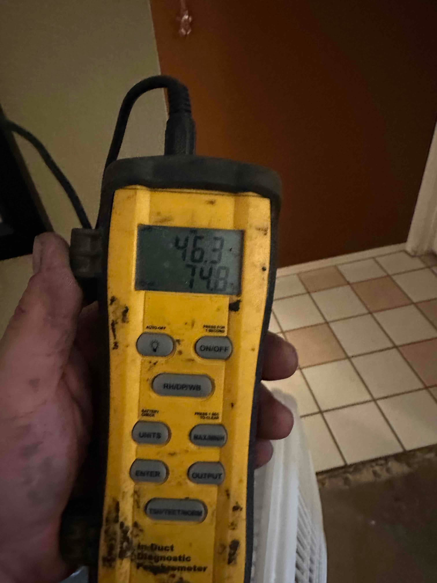 Handheld digital thermometer shows 74.8 degrees, documenting return air temperature during commissioning.