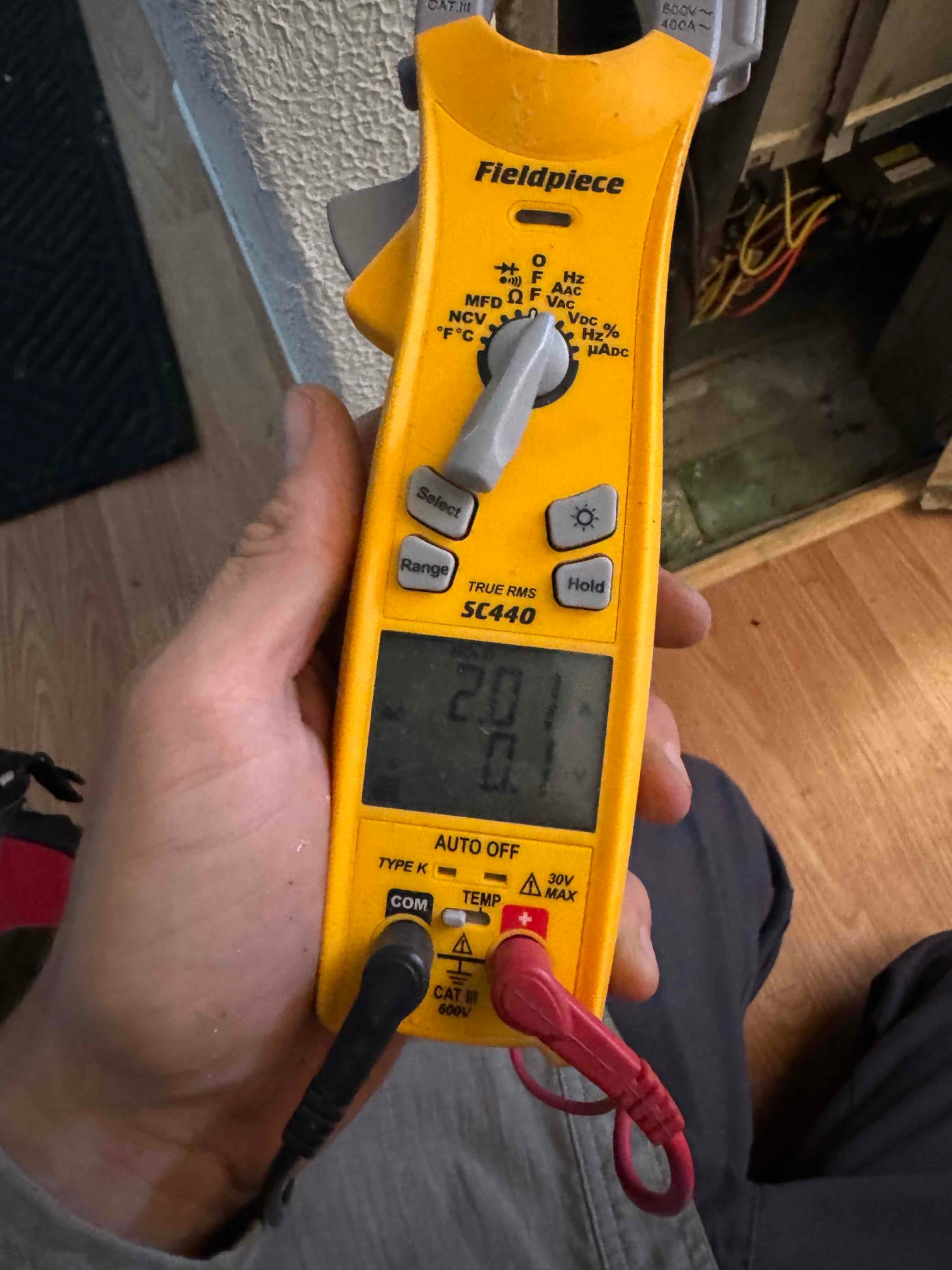 Handheld multimeter measures capacitance across a capacitor, displaying 2.1 μF on the screen with probes connected.
