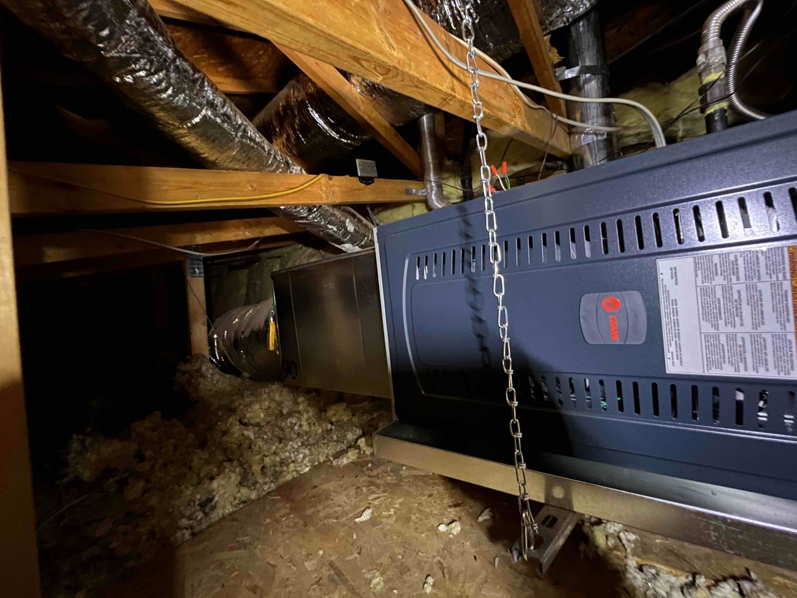 Horizontal gas furnace hung from joists with duct connections and insulated flexible ducts in an attic space.