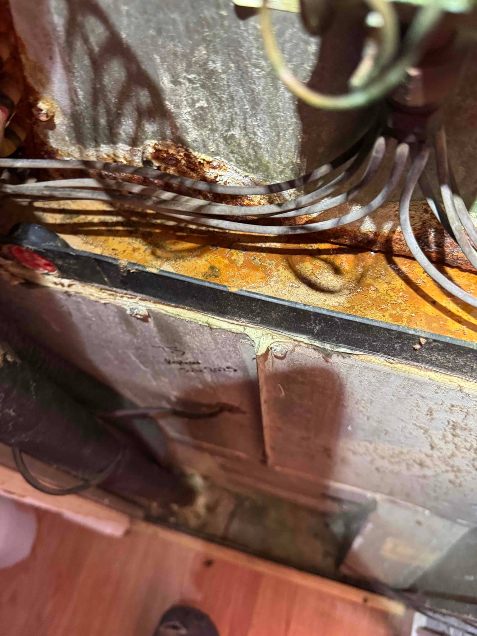 Indoor air handler base shows heavy rust and corrosion around the drain area with multiple control wires routed along the panel.