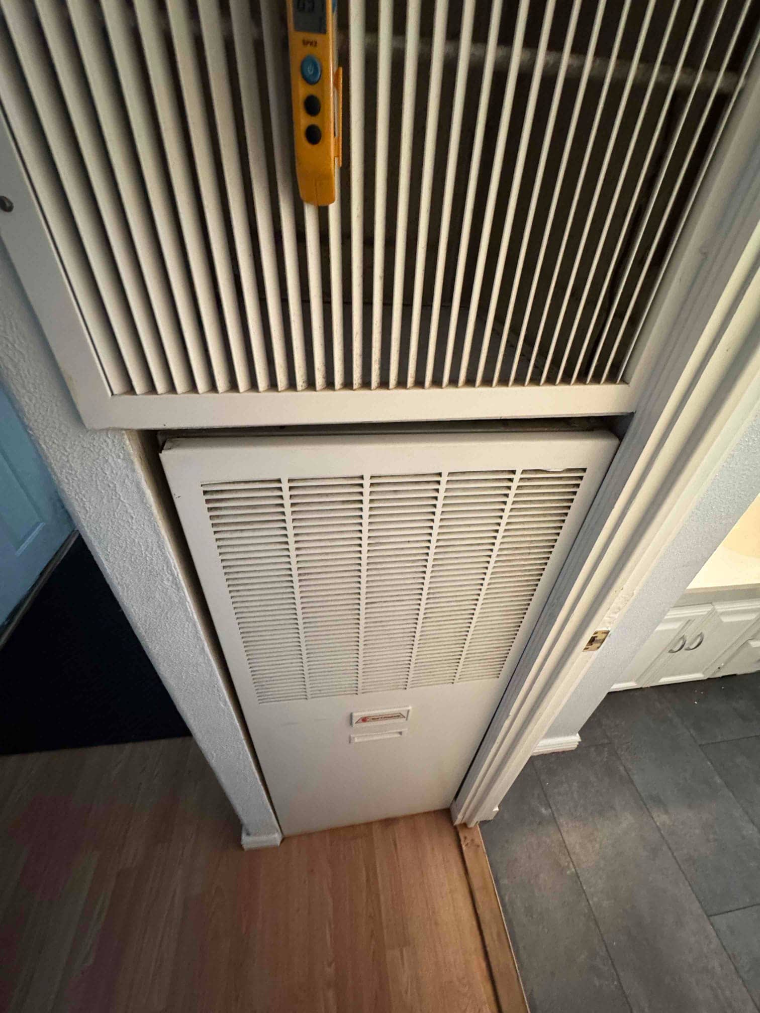 Indoor air handler closet with louvered return grilles and surrounding trim, showing access door closed and adjacent hallway flooring.