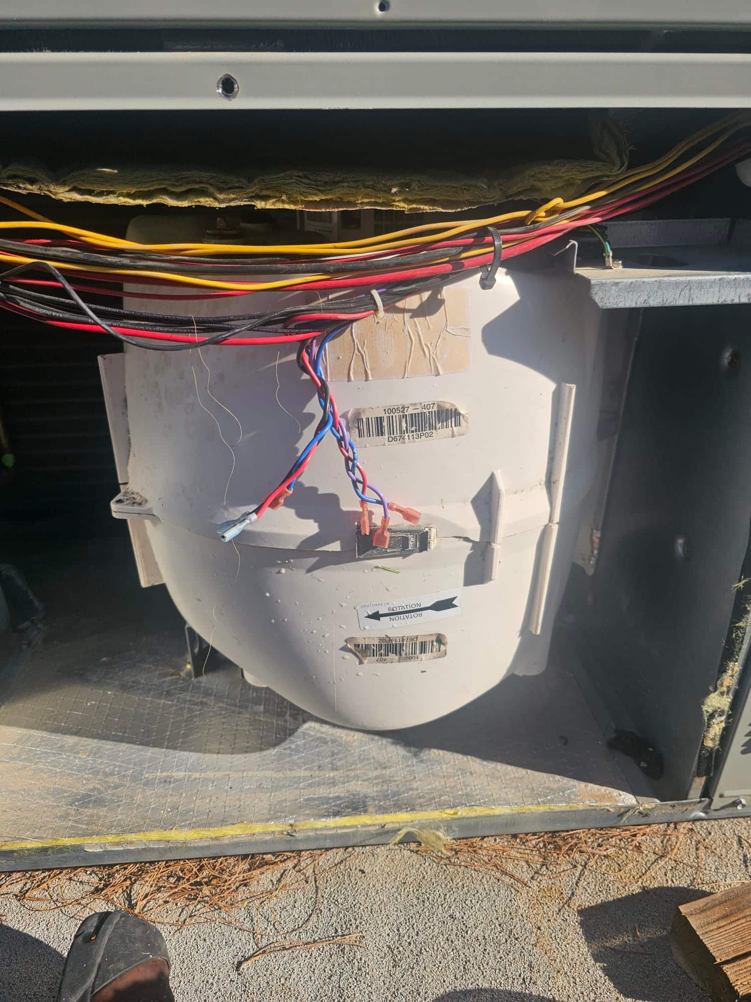 Indoor blower housing exposed with wiring harness connected, showing dust buildup on the housing and adjacent insulation.