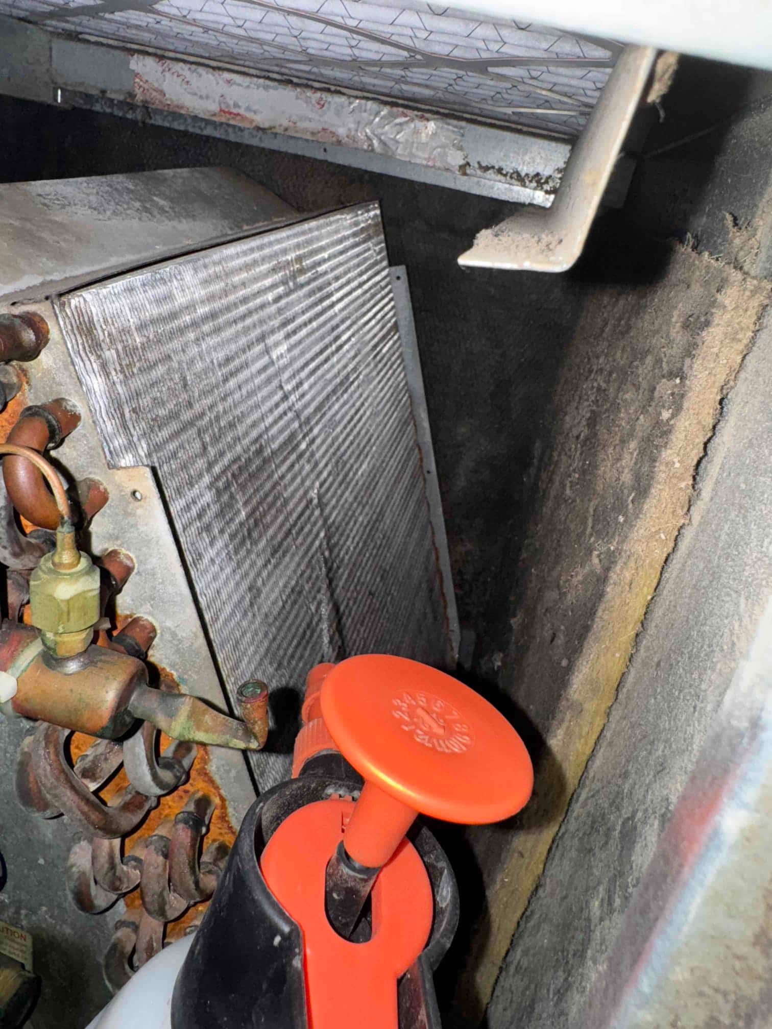 Indoor evaporator coil and copper refrigerant tubing with surface rust visible, next to a red service access handle inside the air handler.