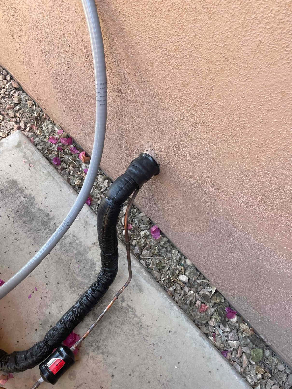 Insulated refrigerant line set and liquid line with filter-drier exit the wall, alongside flexible electrical conduit at the outdoor unit location.
