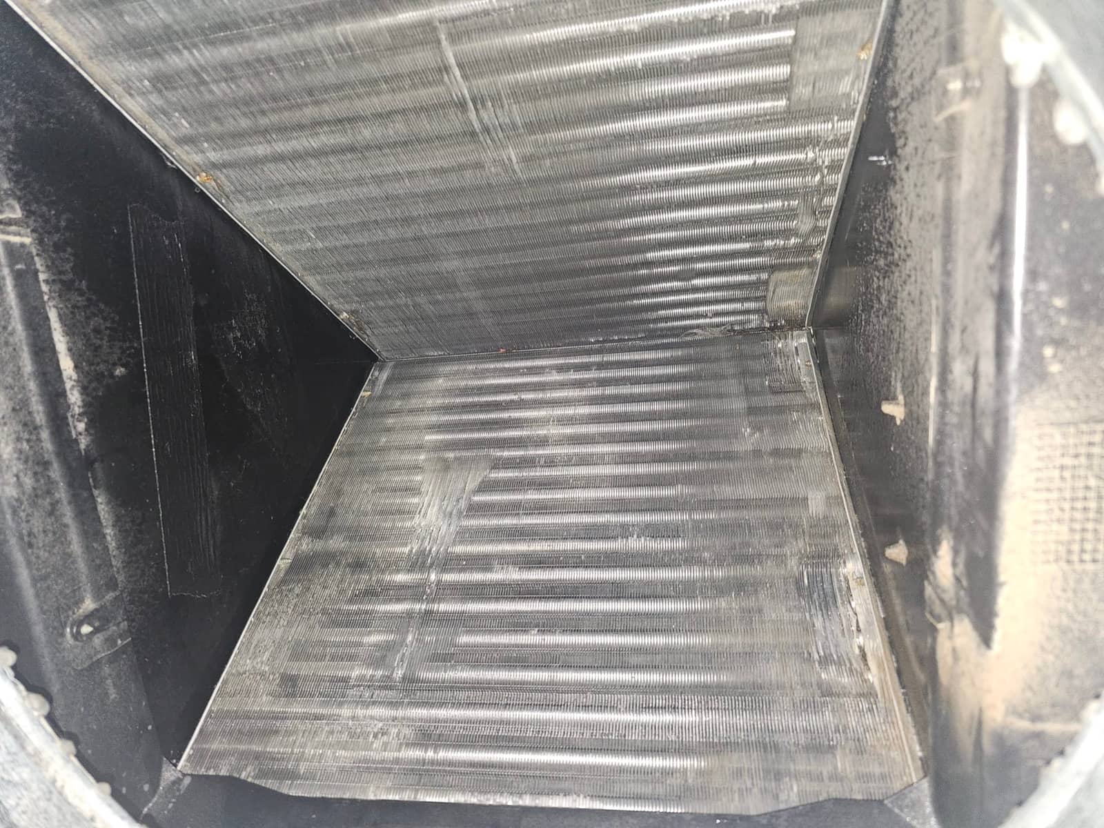 Interior view of an evaporator A-coil, showing V-shaped aluminum fins and surrounding air handler cabinet.