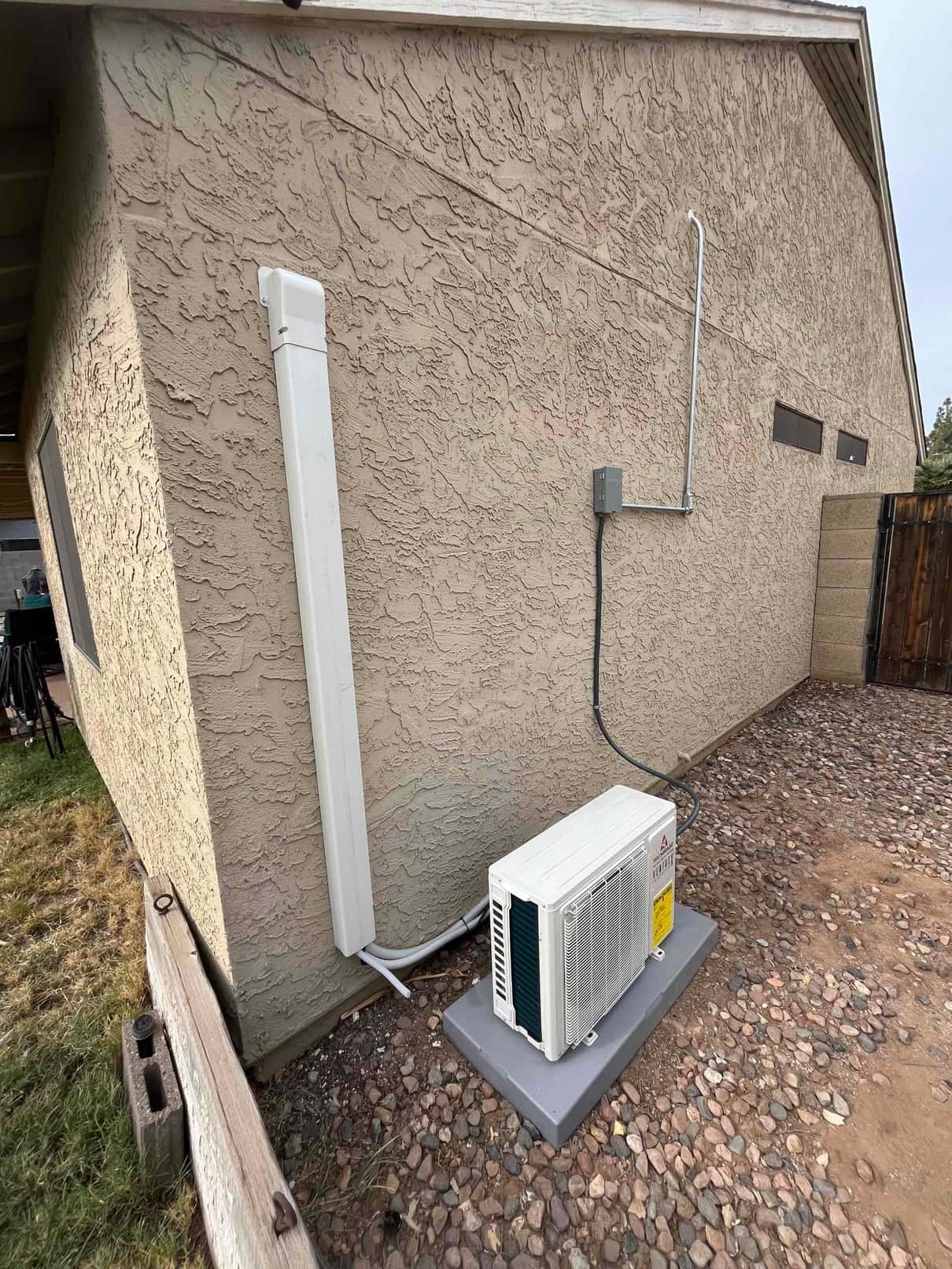 Mini-split outdoor condenser set on a level pad with line-hide, insulated refrigerant lines, and exterior electrical whip and disconnect.
