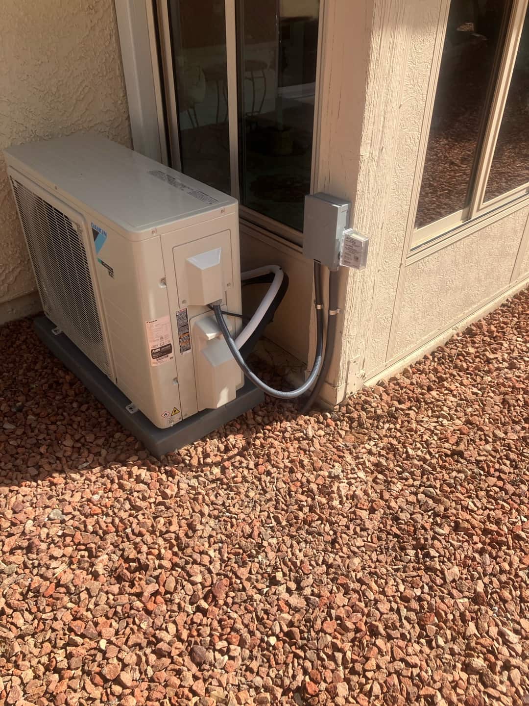 Mini-split outdoor unit set on a level pad with insulated line set and weatherproof electrical disconnect mounted nearby.