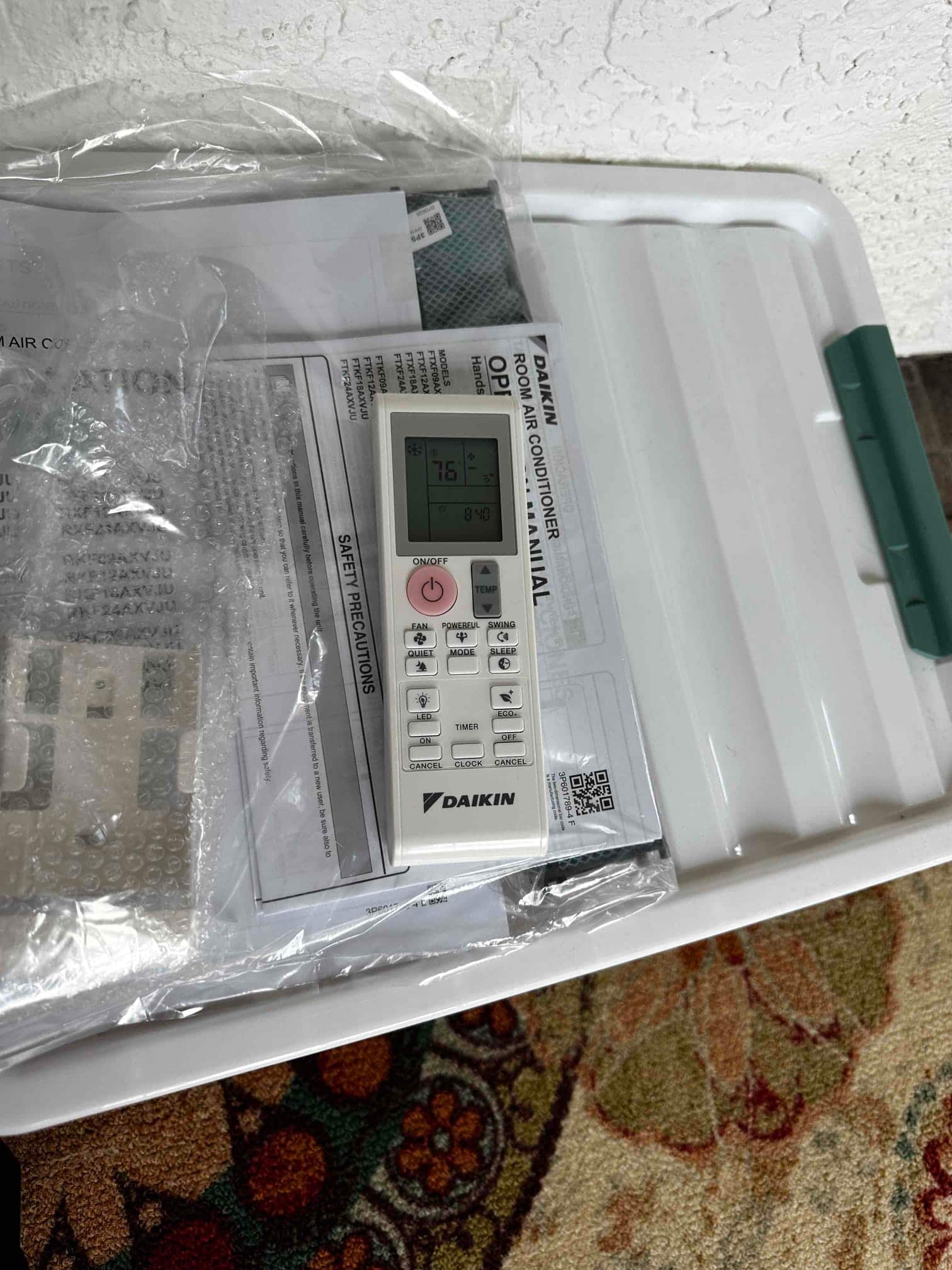 Mini-split remote control with manuals and accessories laid out after installation, showing 76°F on the display.