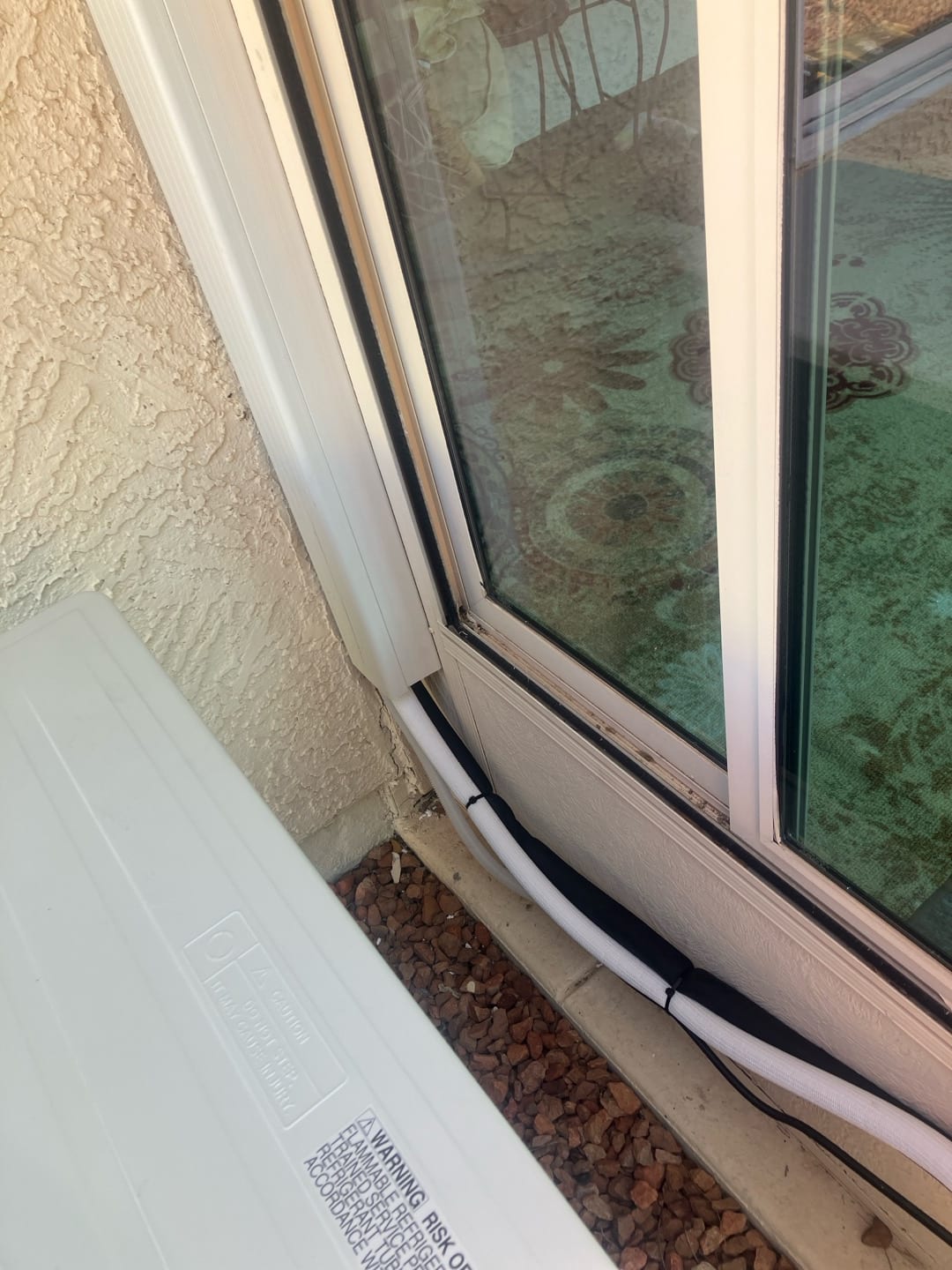 Neatly routed insulated line set and drain exiting a line-hide next to a sliding door beside the outdoor unit.