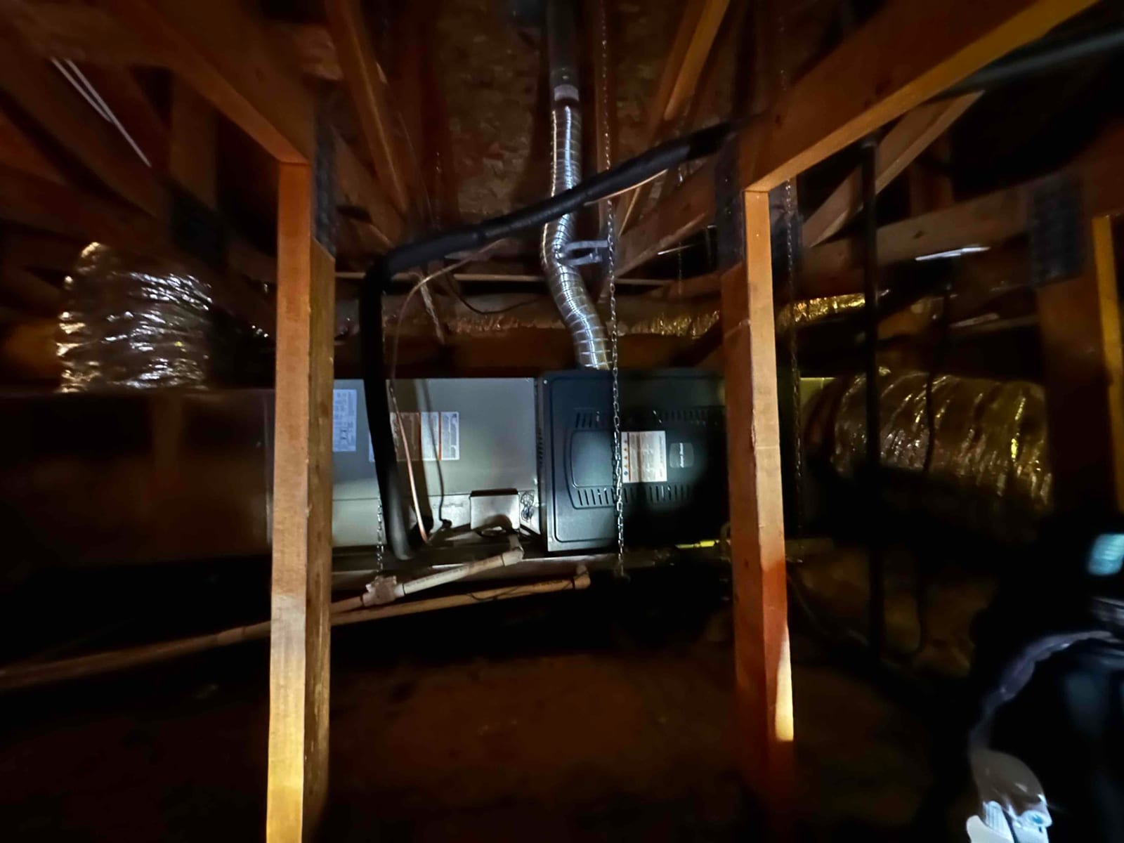 New air handler suspended in the attic with insulated refrigerant lines, drain piping, and flexible duct connections visible.