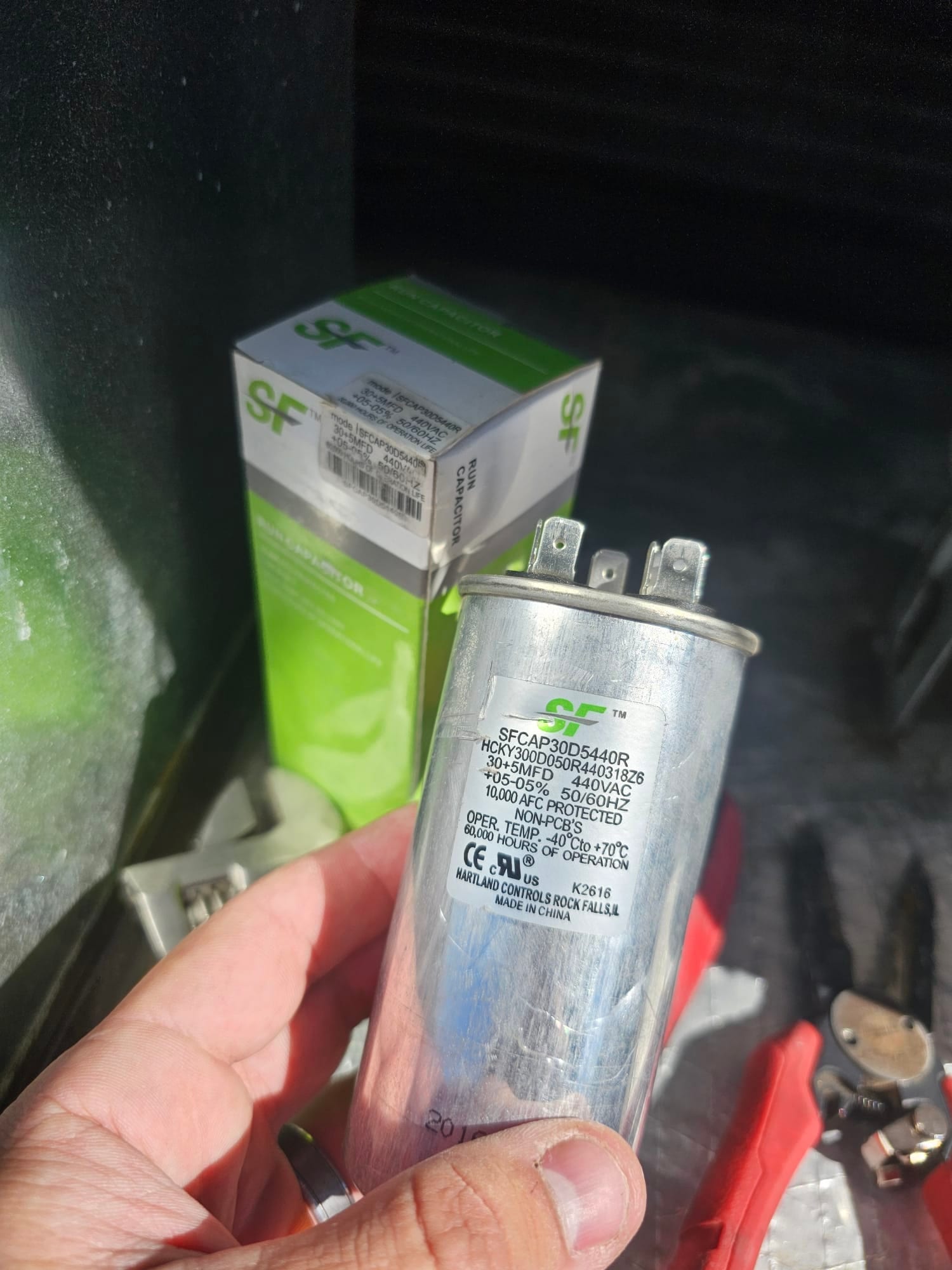 New dual-run capacitor held in hand on the service platform, labeled 30/5 μF and 440 VAC with clearly printed specifications.