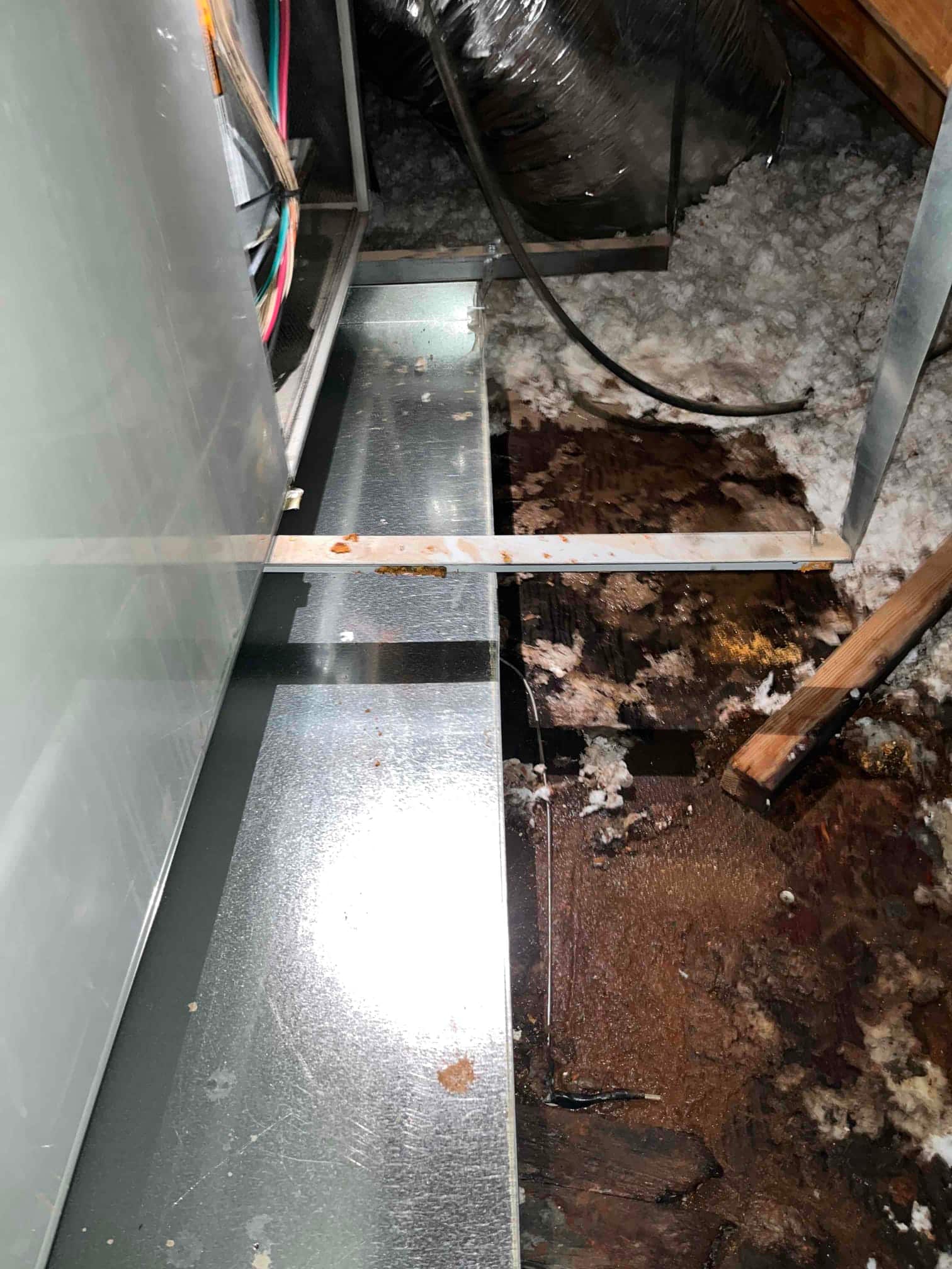 New galvanized condensate drain pan installed in attic beneath air handler, with surrounding wet and stained insulation and decking visible.