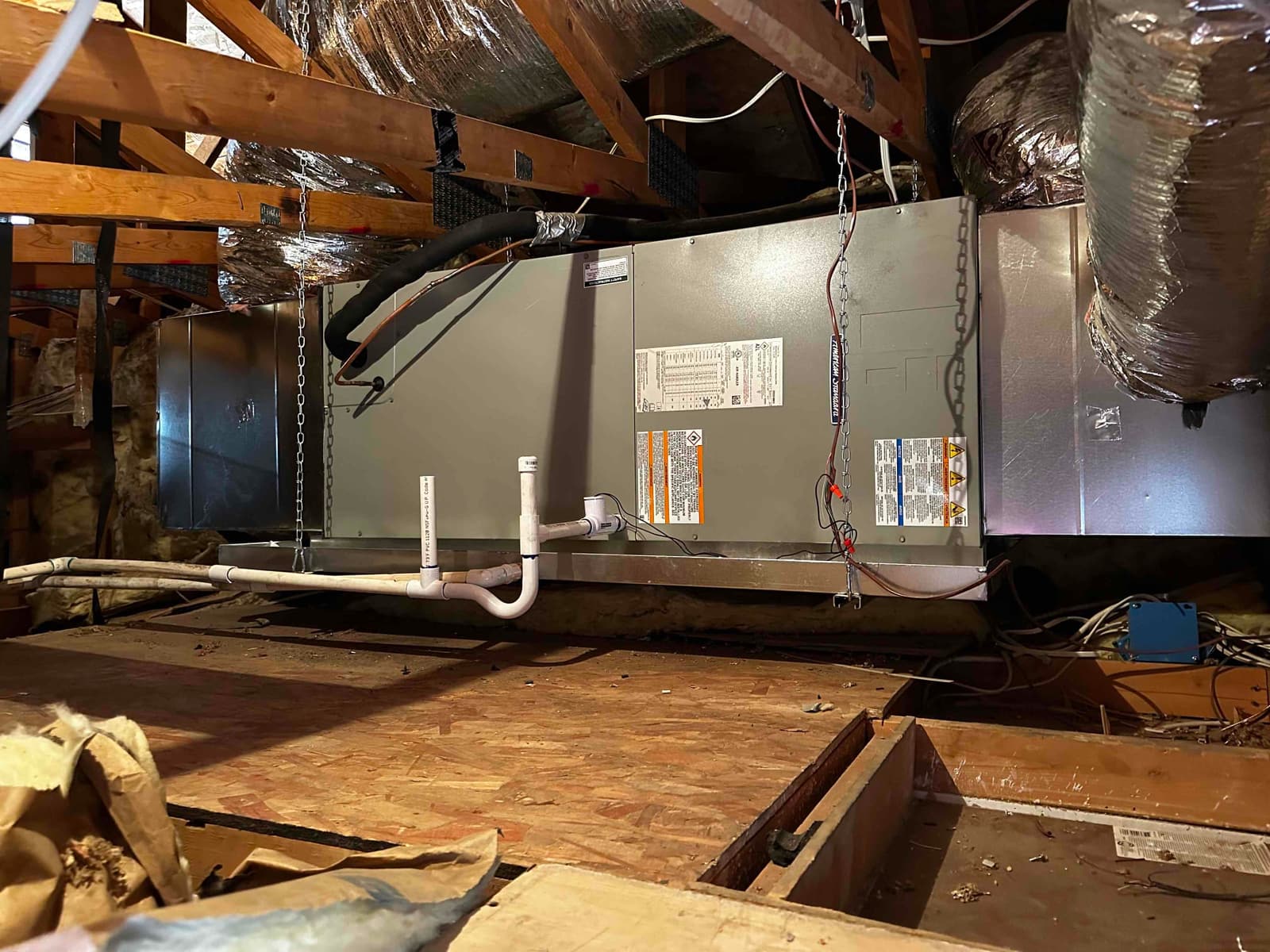 New horizontal air handler suspended in attic with insulated ducts connected and PVC condensate drain routed to the secondary pan.