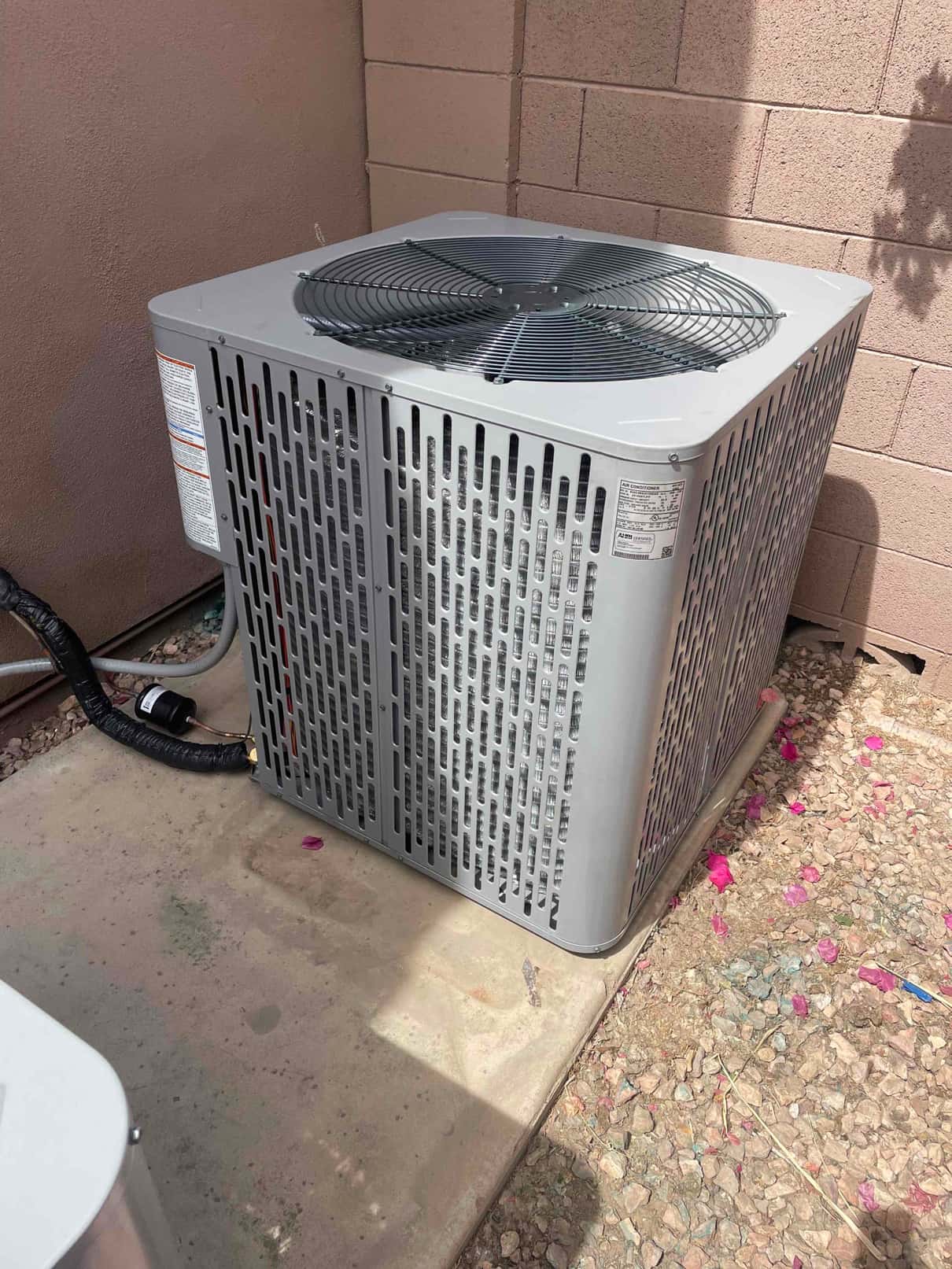 New outdoor condenser set on a concrete pad with insulated refrigerant lines routed to the wall penetration.