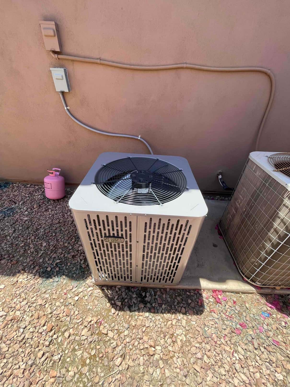 New outdoor condenser set on a level pad with electrical whip and disconnect mounted on the wall beside it.