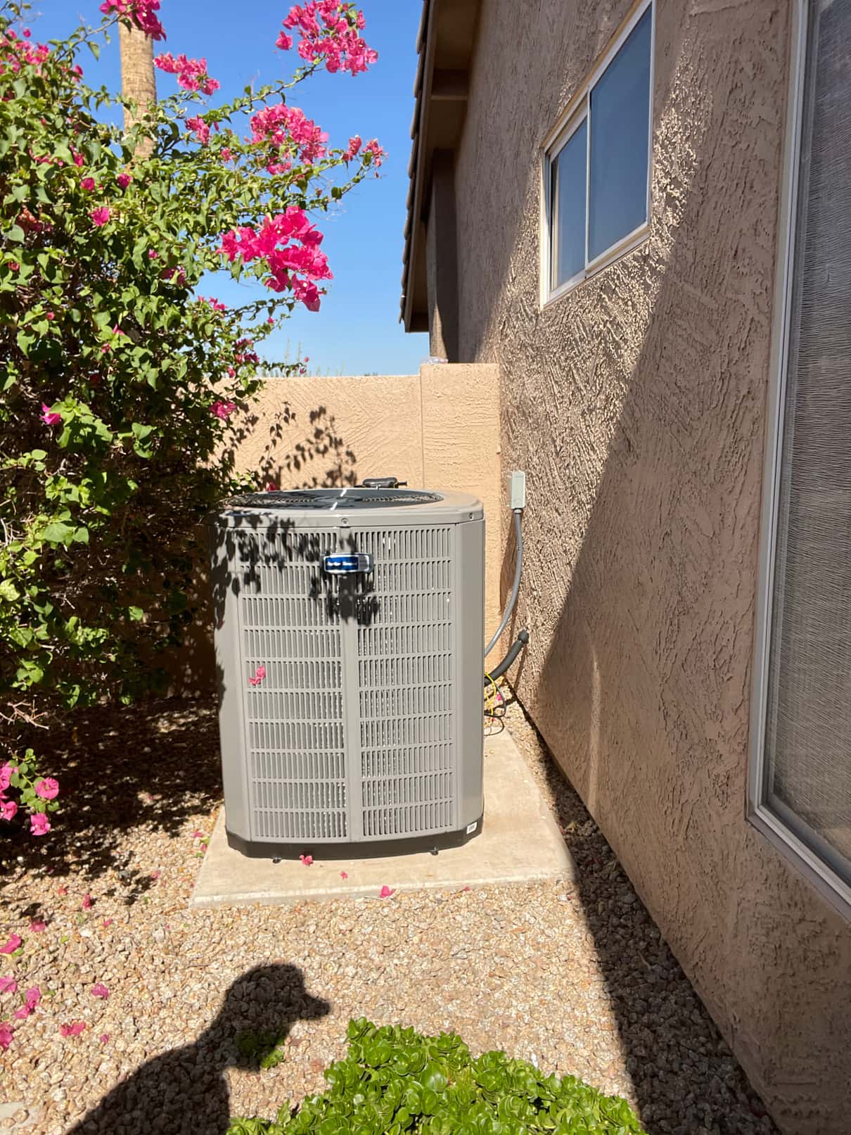 New outdoor condenser set on a level pad with insulated line set and electrical disconnect mounted on the wall.