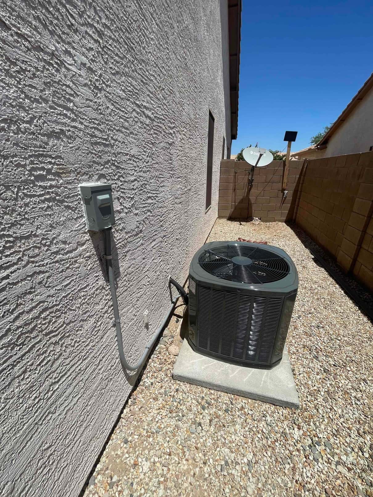 New outdoor condenser set on a level pad with insulated line set and mounted electrical disconnect along the exterior wall.
