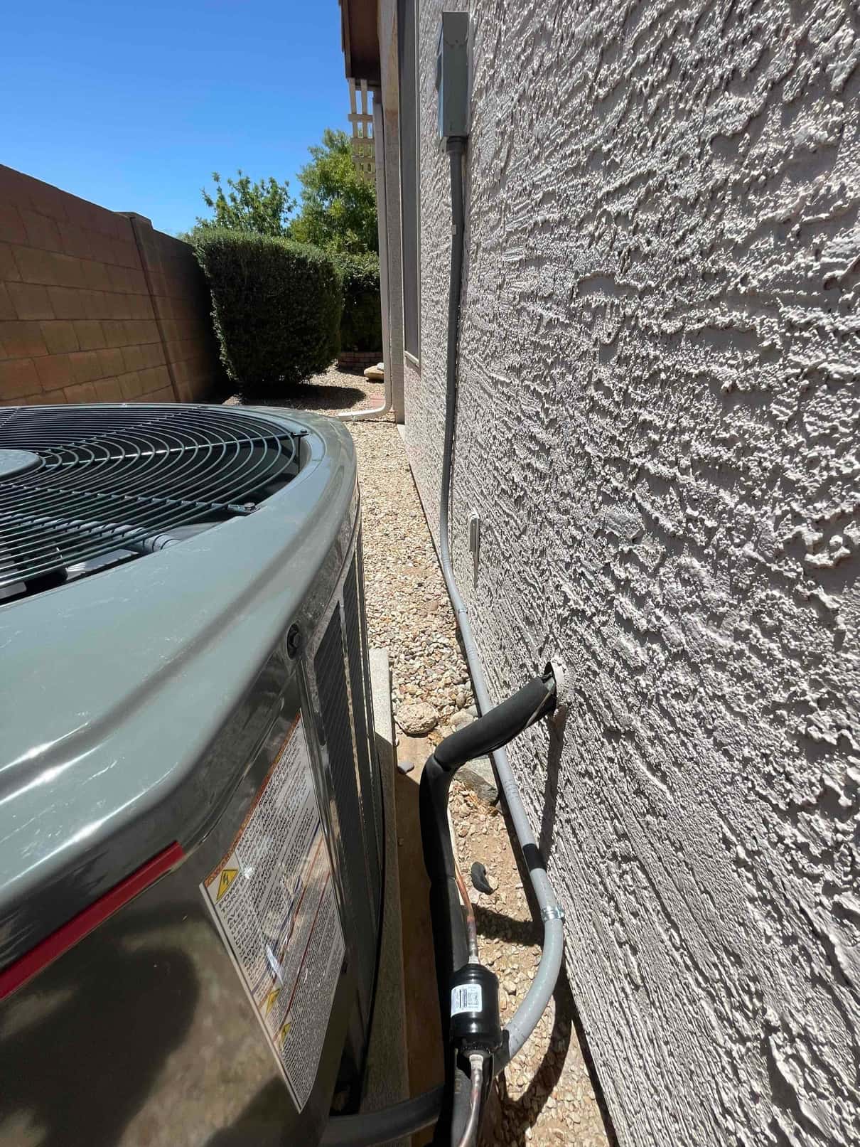 New outdoor condenser set on a level pad with insulated refrigerant line set and electrical whip routed to the wall disconnect.