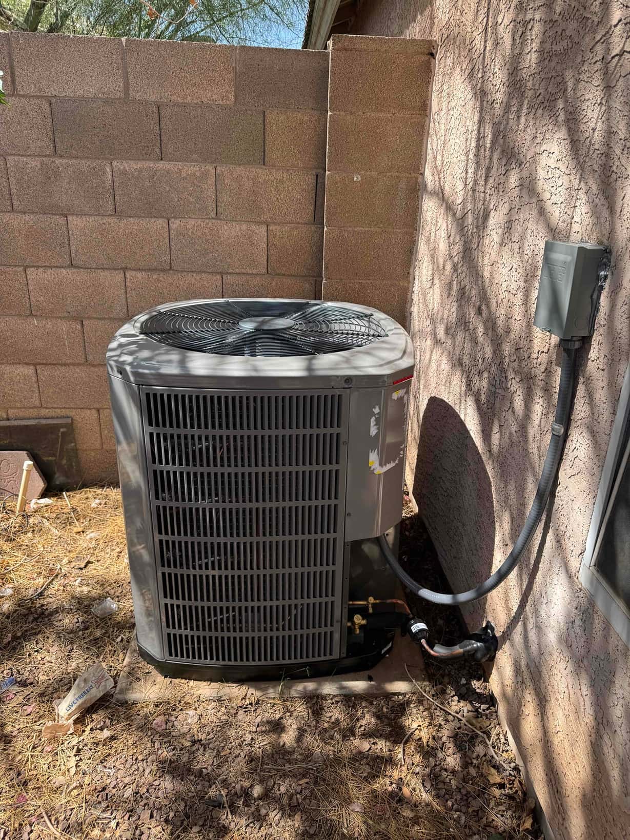 New outdoor condenser set on a level pad with insulated refrigerant lines and weatherproof disconnect mounted on the wall.