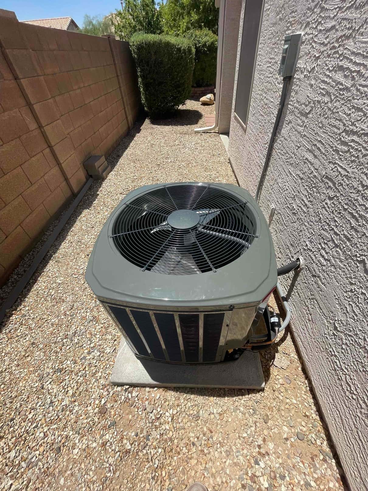 New outdoor condenser set on a level pad with insulated refrigerant lines and exterior disconnect mounted on the wall.