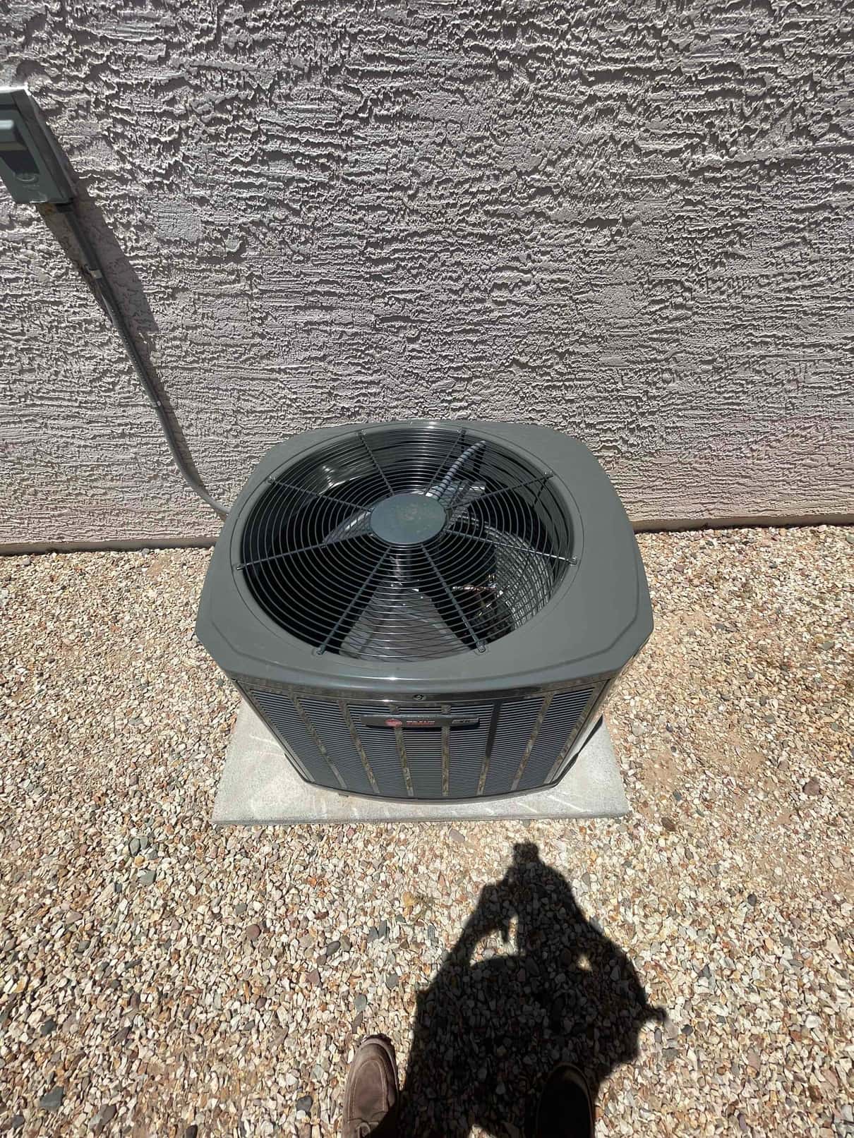 New outdoor condenser set on a level pad with nearby electrical disconnect, placed on a gravel area beside the house.