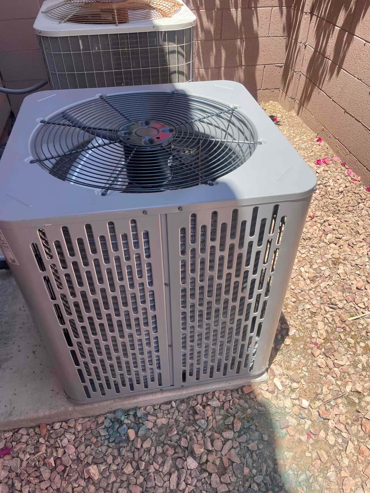 New outdoor condenser set on a level pad with protective grille, next to an older unit in the service area.