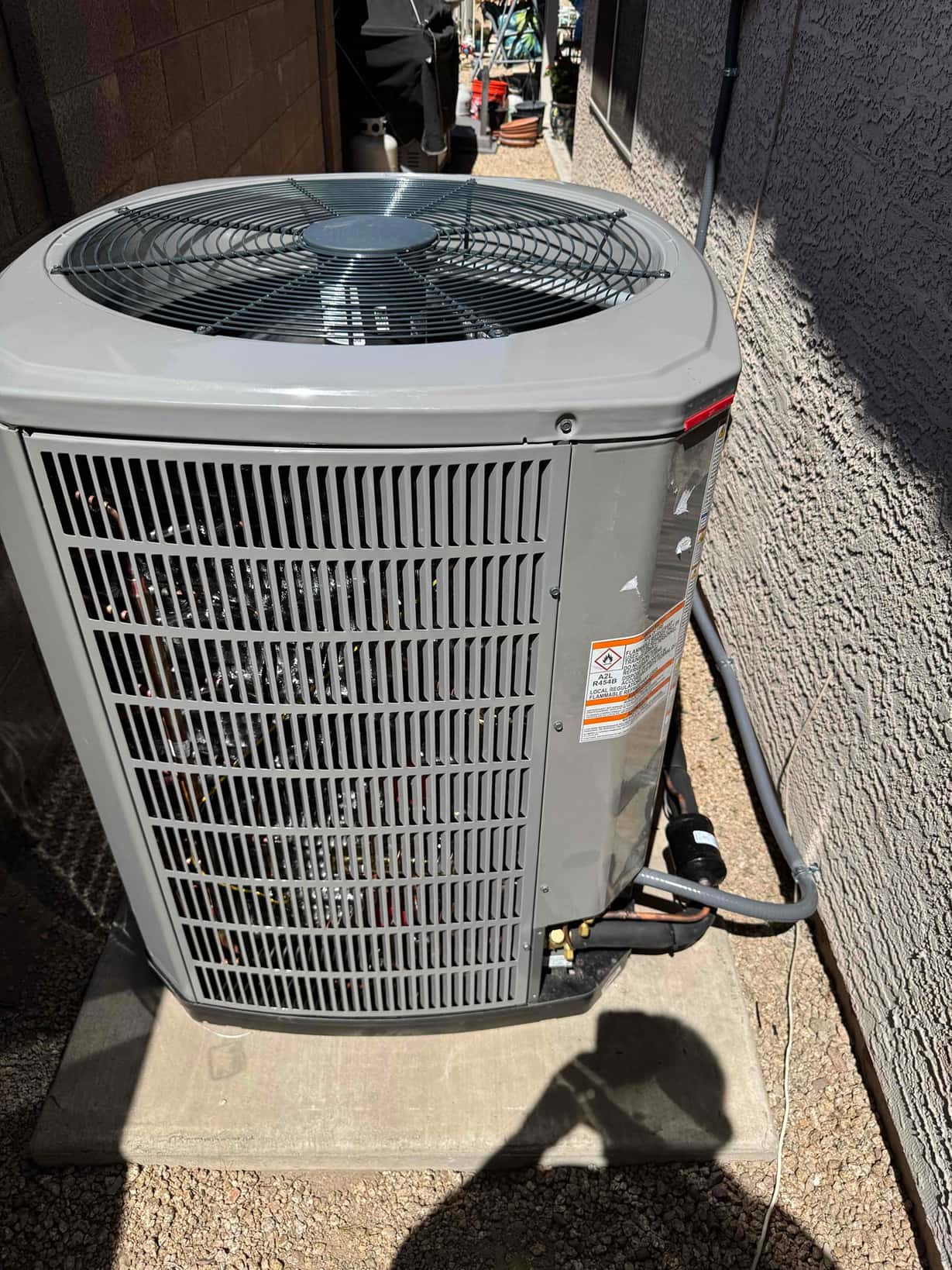 New outdoor heat pump condenser set on a level pad with insulated line set, filter drier, and electrical whip connected.