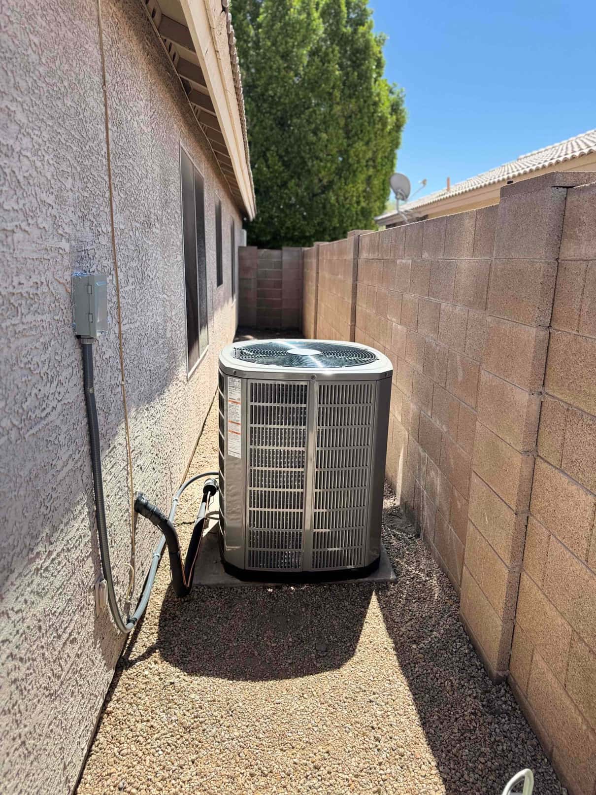 New outdoor heat pump condenser set on a level pad with insulated refrigerant lines and electrical disconnect mounted on the wall.
