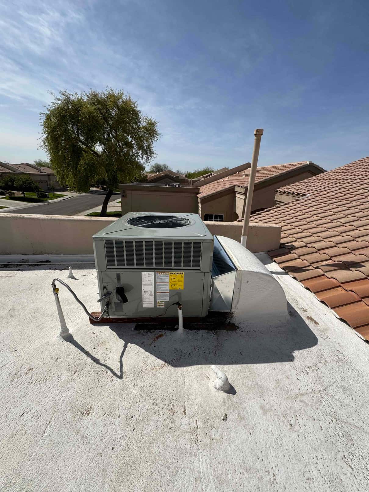 New rooftop package HVAC unit set on curb with connected duct transition, drain, and electrical conduit visible.