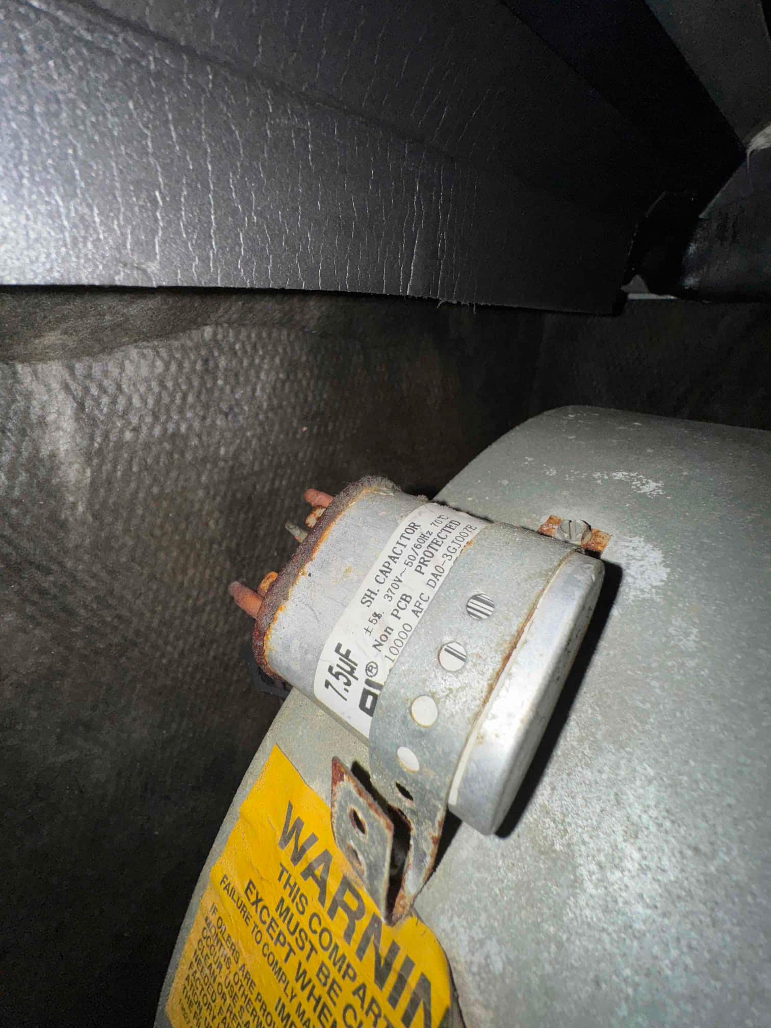 Old cylindrical motor capacitor mounted with a metal strap, showing rust on terminals and printed rating of 7.5 μF.