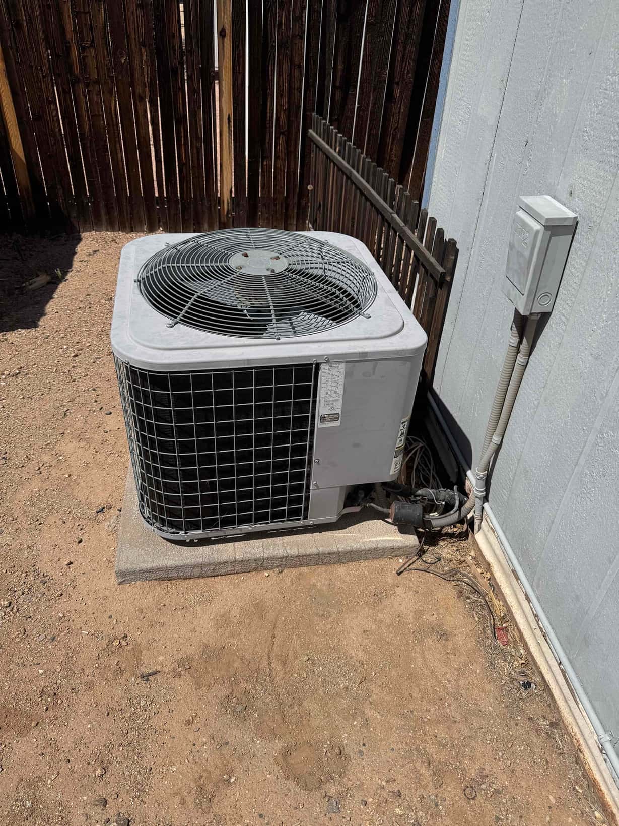 Outdoor air conditioning condenser unit on a concrete pad beside a house, with electrical disconnect and refrigerant lines visible.