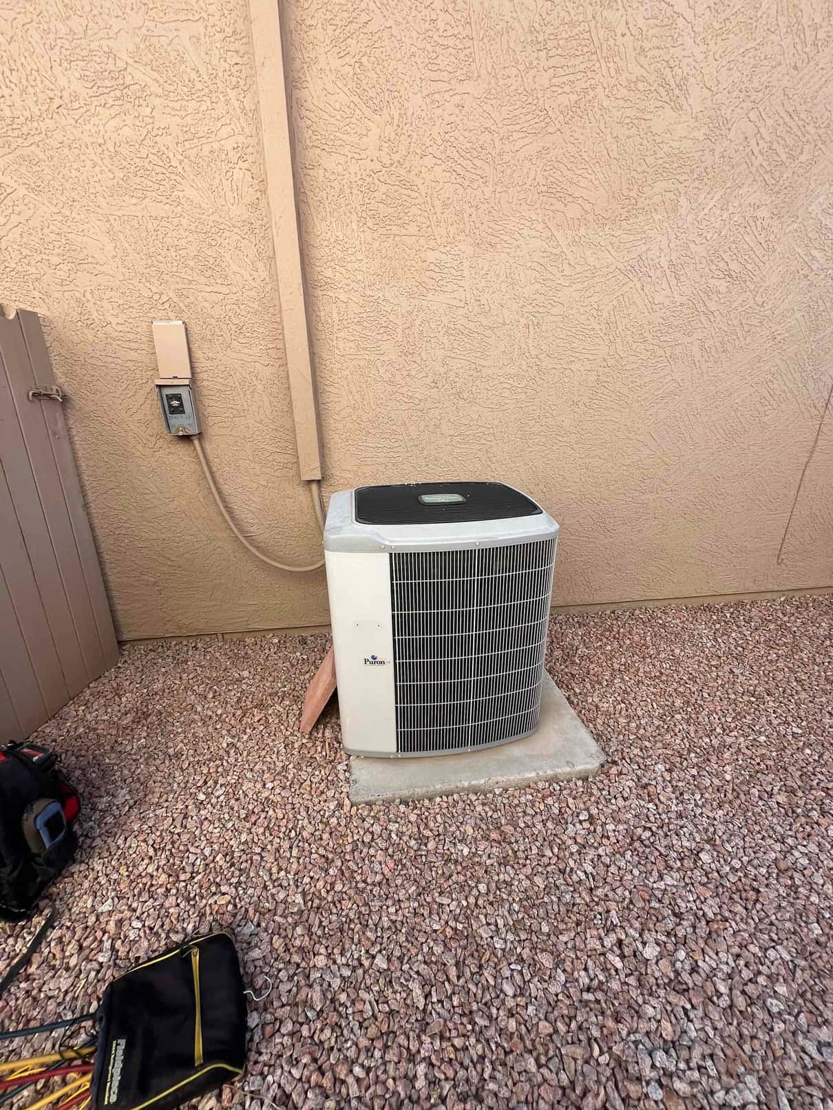 Outdoor air conditioning condenser unit on a concrete pad with electrical disconnect mounted on the adjacent wall.