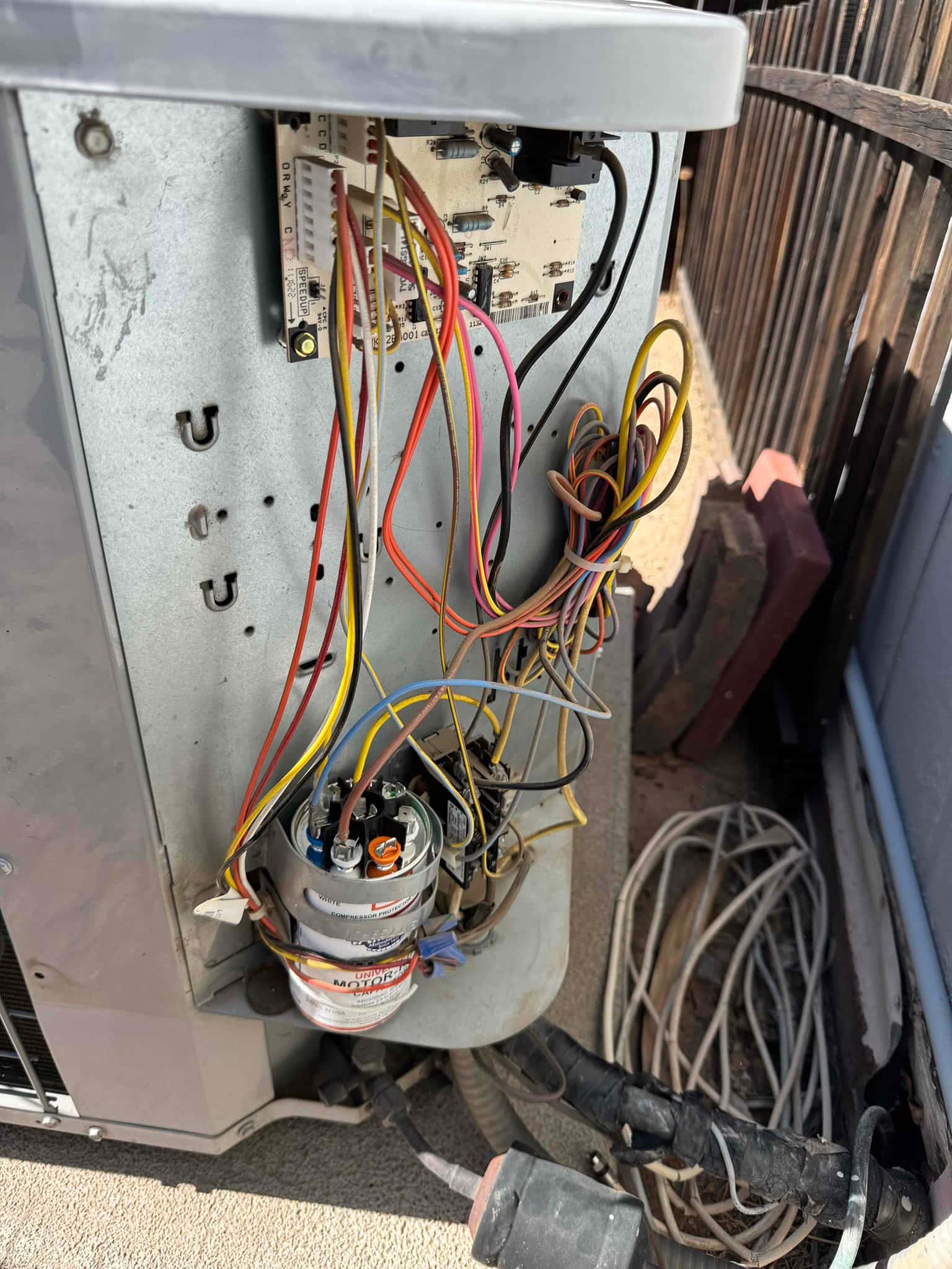 Outdoor condenser control compartment open, showing wiring, contactor, and newly installed run capacitors with connected terminals and leads.