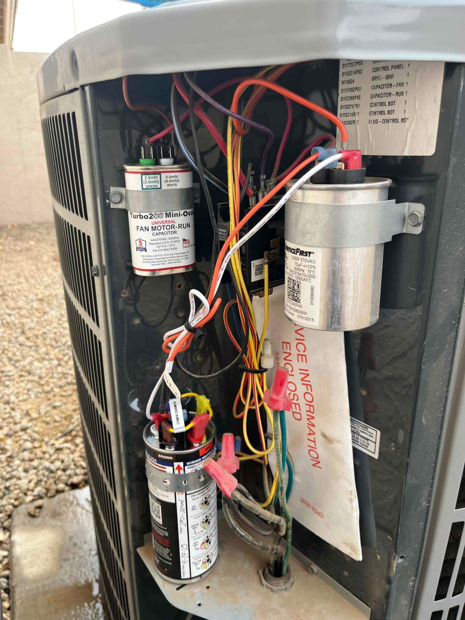 Outdoor condenser electrical compartment shows new start assist kit and dual-run capacitors installed with connected wiring and terminals.