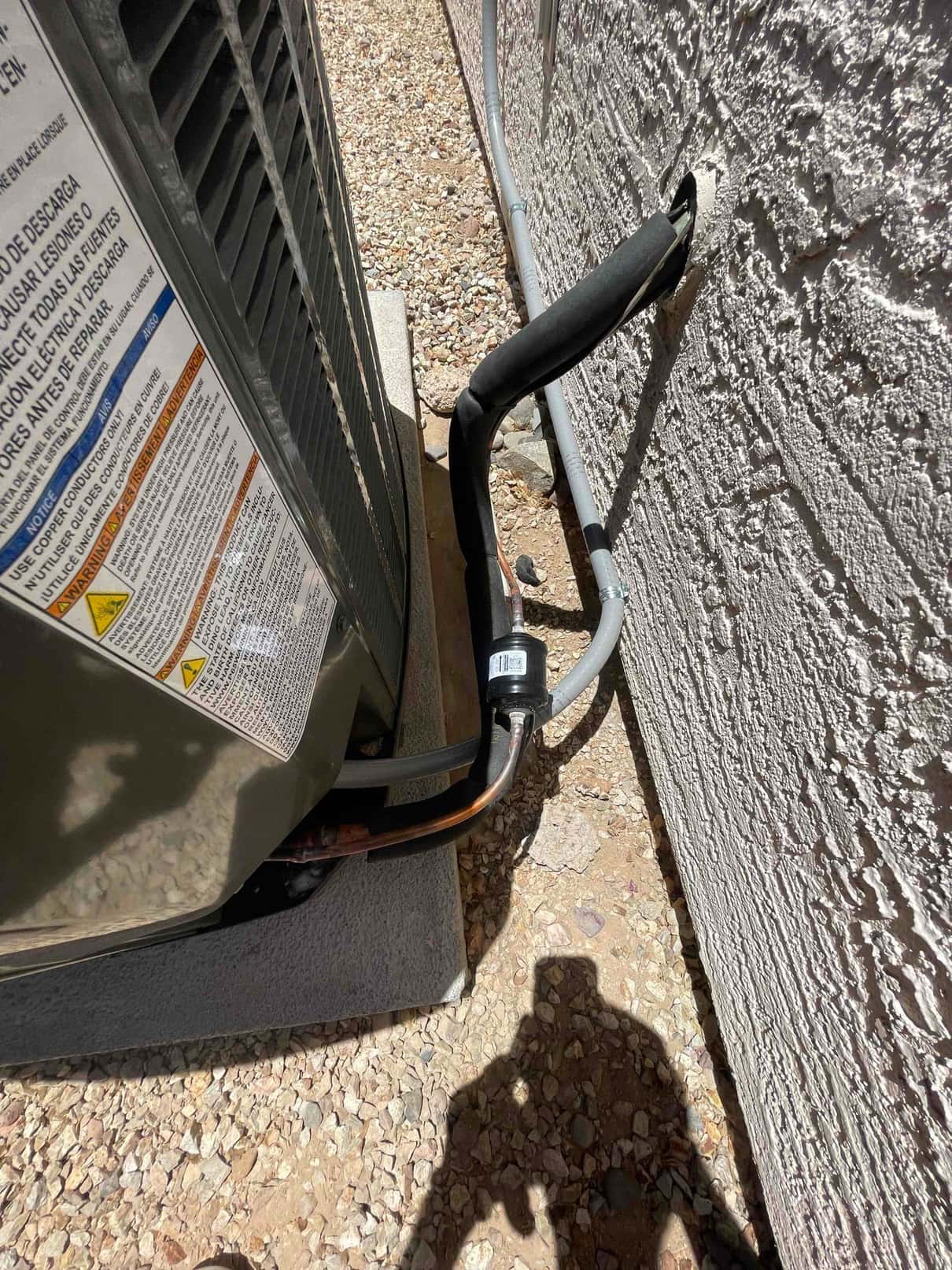 Outdoor condenser set on a level pad with insulated refrigerant line set and electrical conduit entering the wall penetration.