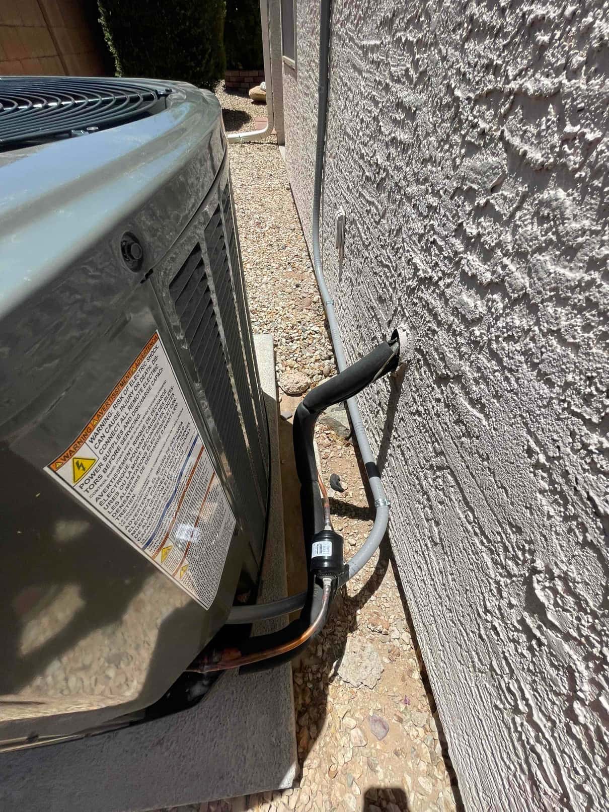 Outdoor condenser set on a level pad with insulated refrigerant lines and electrical conduit routed along the exterior wall.