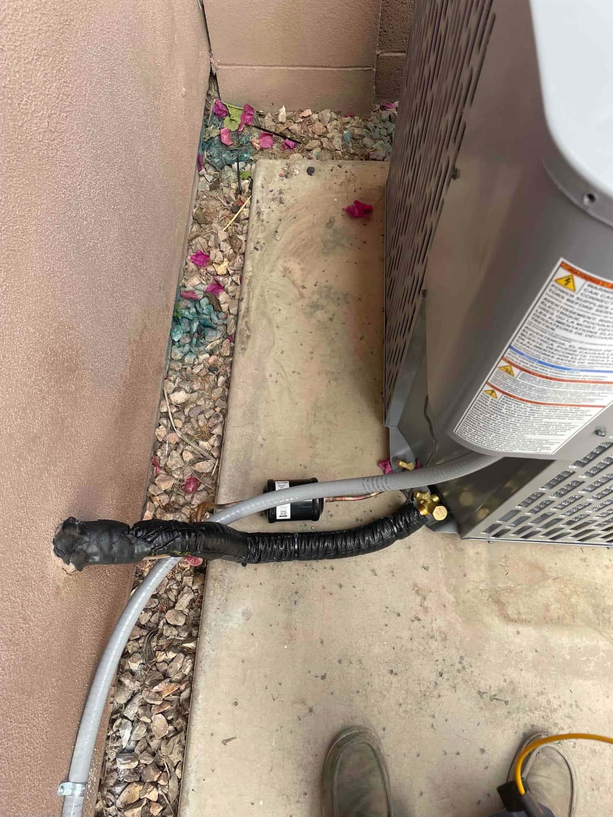 Outdoor condenser set on a pad with insulated refrigerant lines, service valves, and electrical whip neatly routed to the unit.