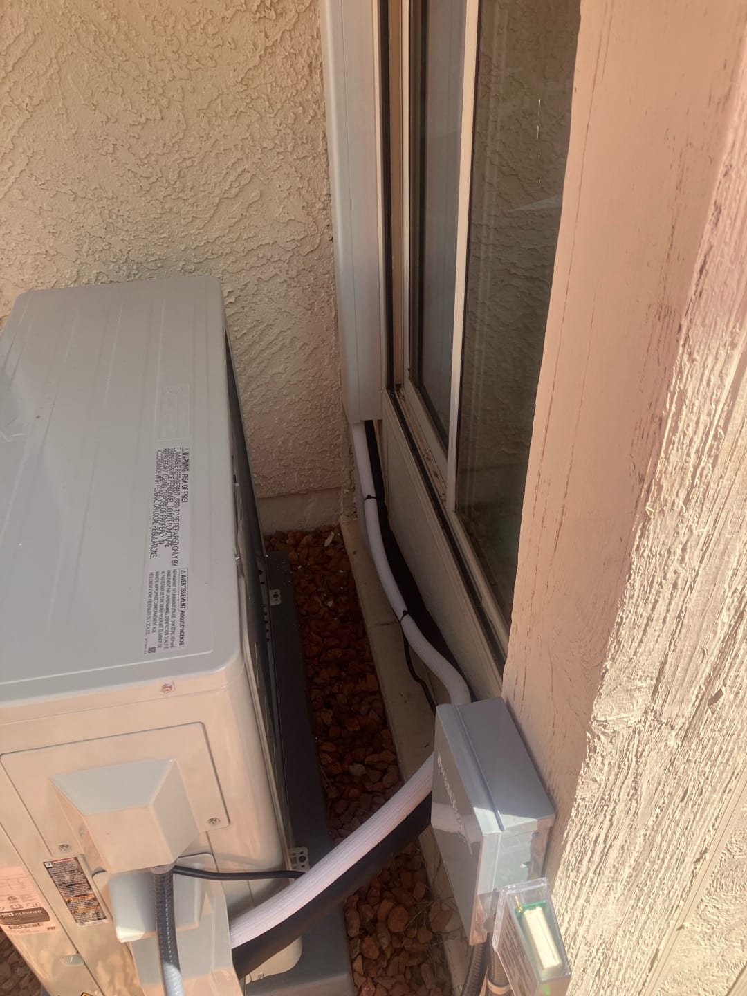 Outdoor mini-split condenser set on a pad with insulated line set in cover and weatherproof electrical disconnect mounted nearby.