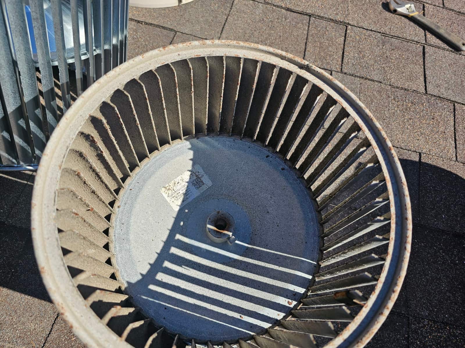 Removed blower wheel sits on a rooftop, showing dust accumulation on blades and hub area before cleaning or replacement.