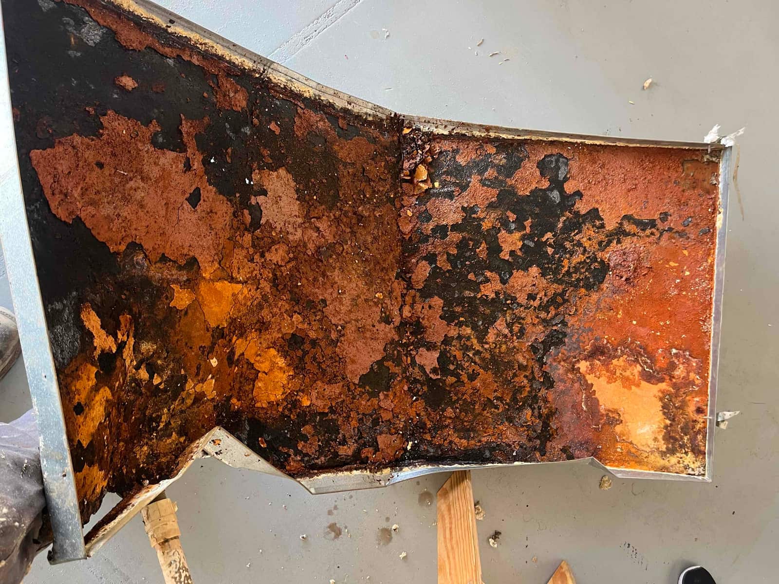 Removed condensate drain pan shows extensive rust, corrosion, and perforation across the metal surface prior to replacement.