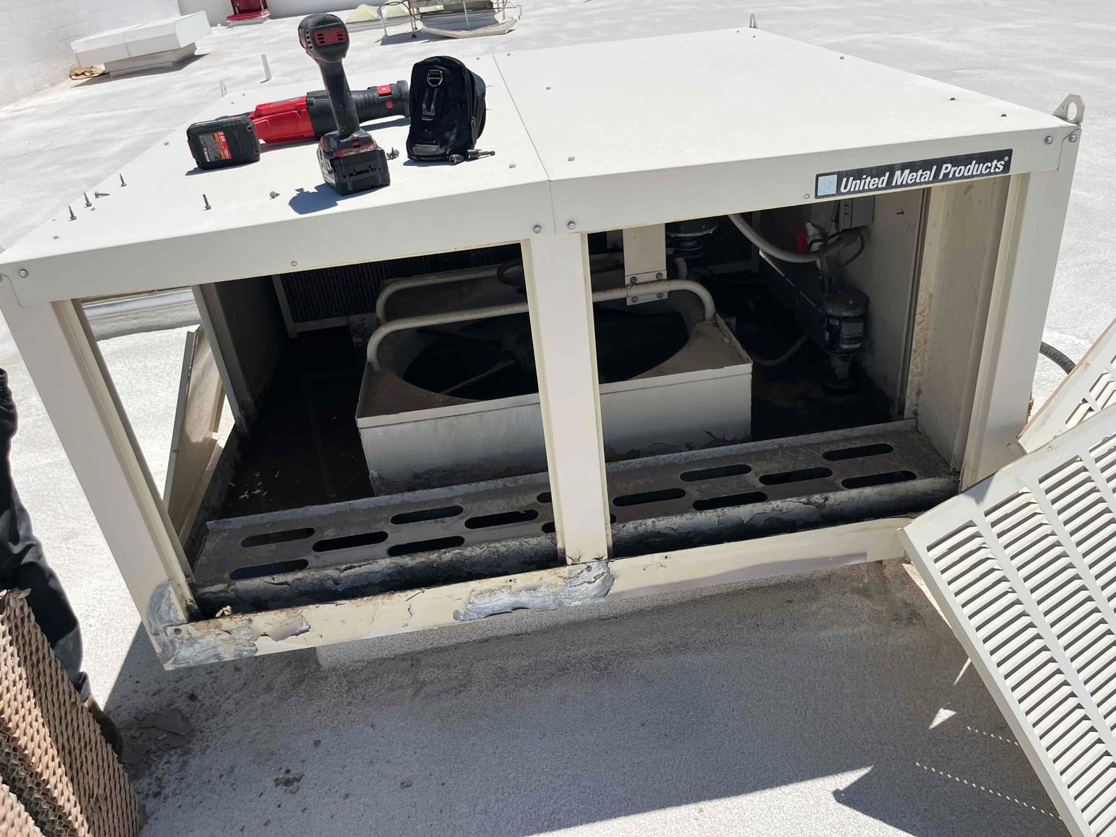 Rooftop evaporative cooler housing opened, showing internal fan section and corroded drain pan with mineral buildup on the base.