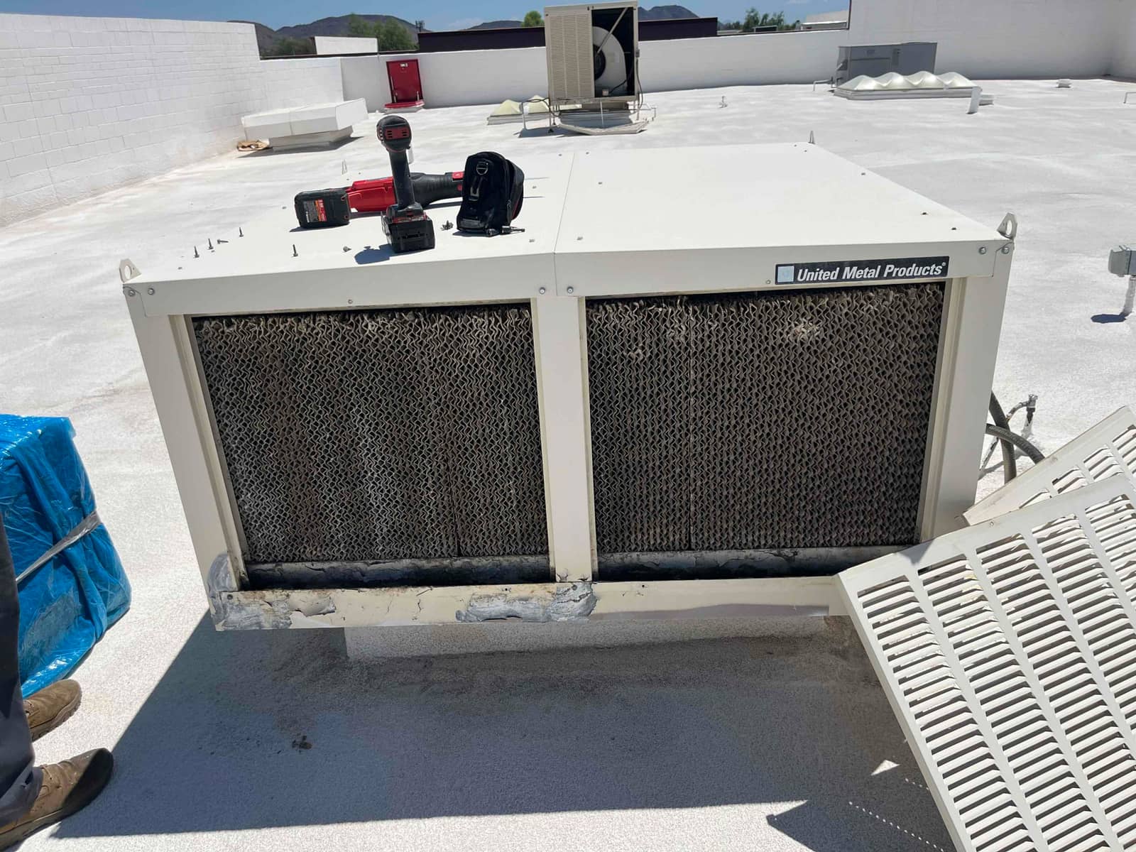 Rooftop evaporative cooler with worn, mineral-encrusted media pads before replacement, showing uneven saturation and buildup across both intake panels.