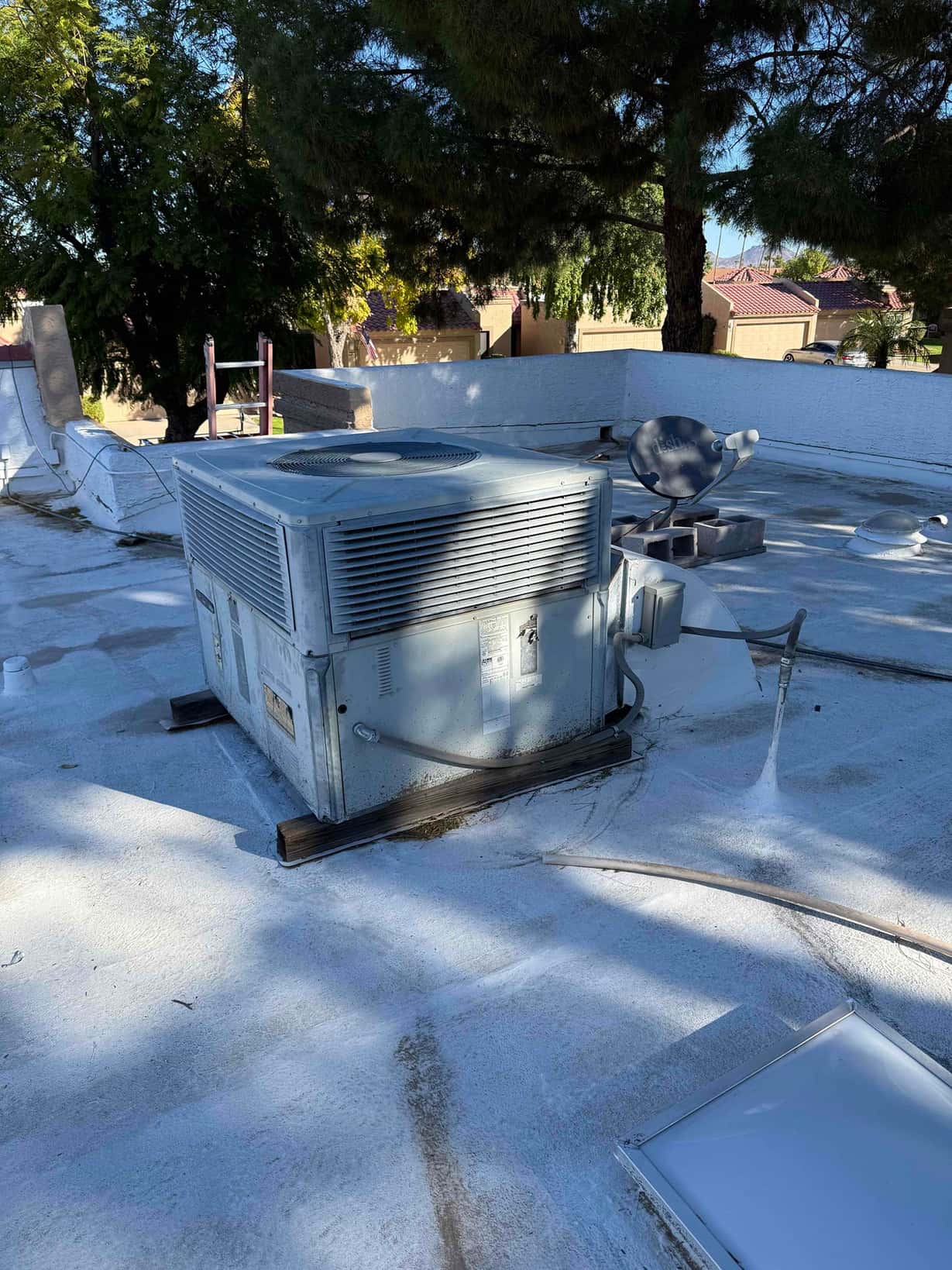 Rooftop package air conditioning unit on a flat roof, with electrical disconnect and conduit visible beside the cabinet.