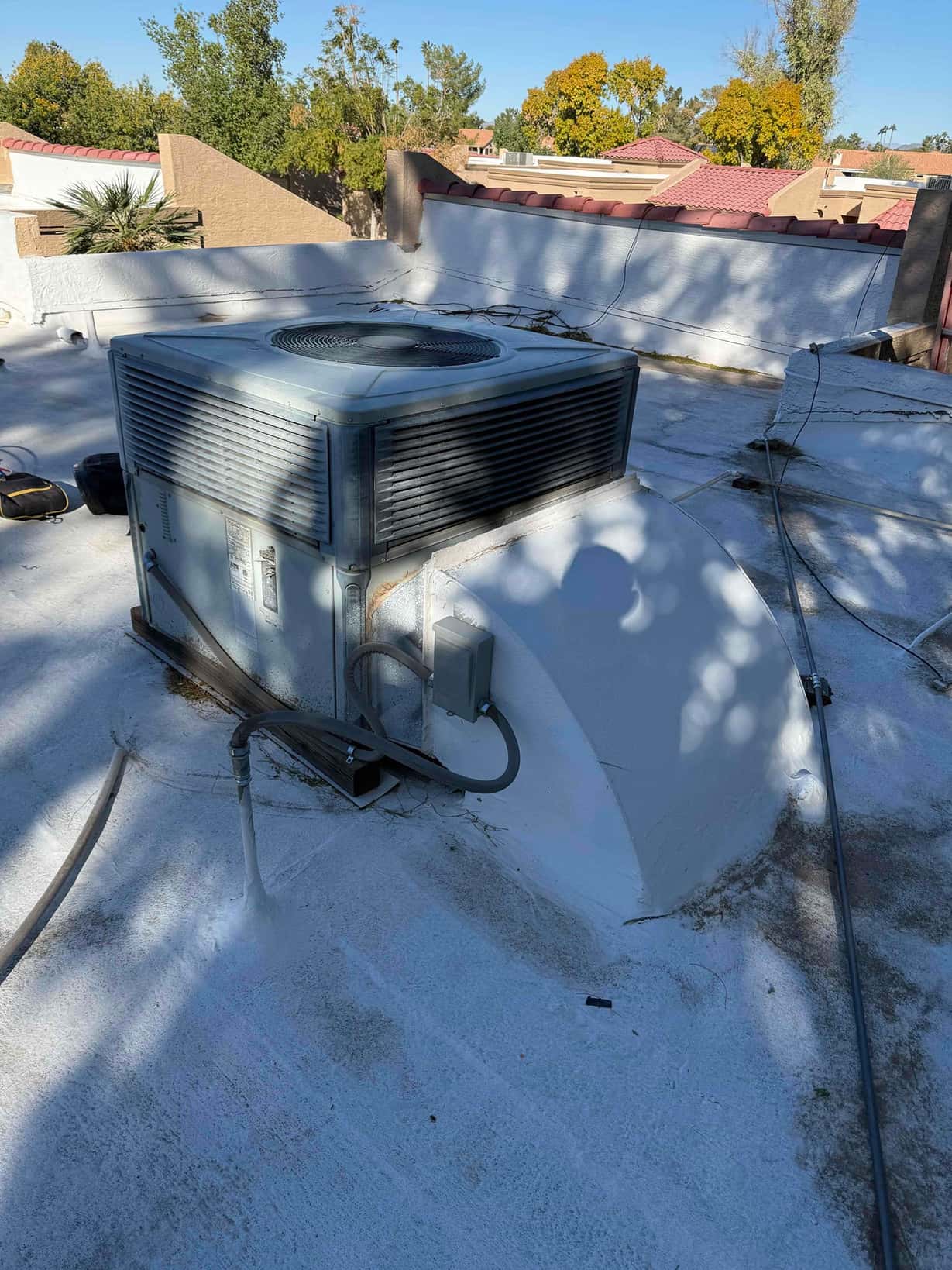 Rooftop packaged air conditioner on a flat roof, showing condenser cabinet, electrical disconnect box, and sealed curb flashing.