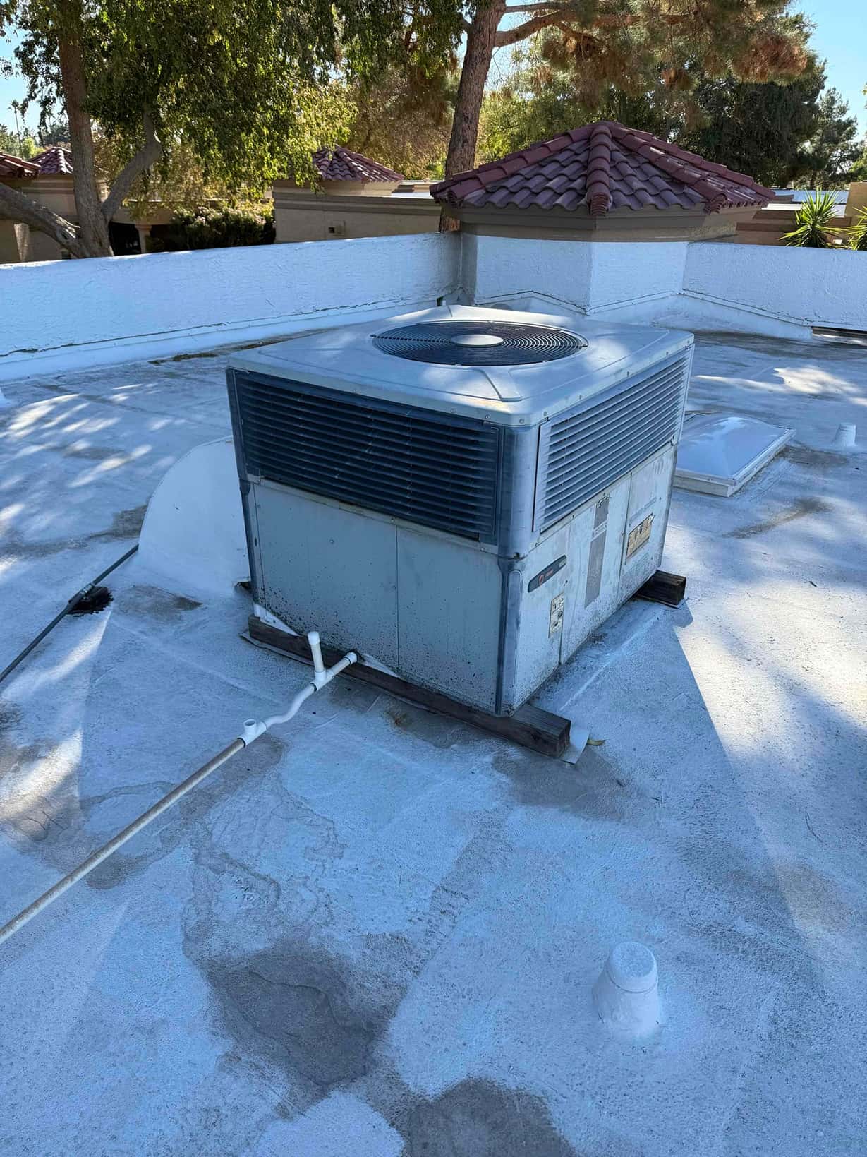 Rooftop packaged air conditioning unit on a flat roof, showing condenser fan grille, weathered panels, and electrical conduit connections.