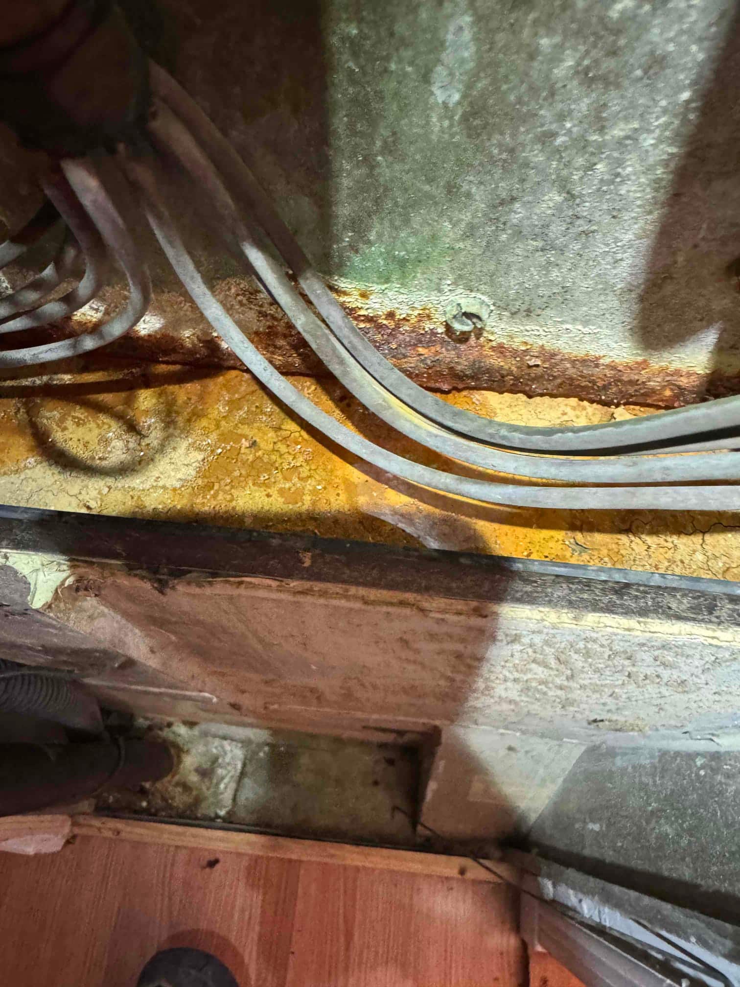 Rust-stained metal surface beneath HVAC cabinet with multiple electrical cables routed along the corroded ledge.