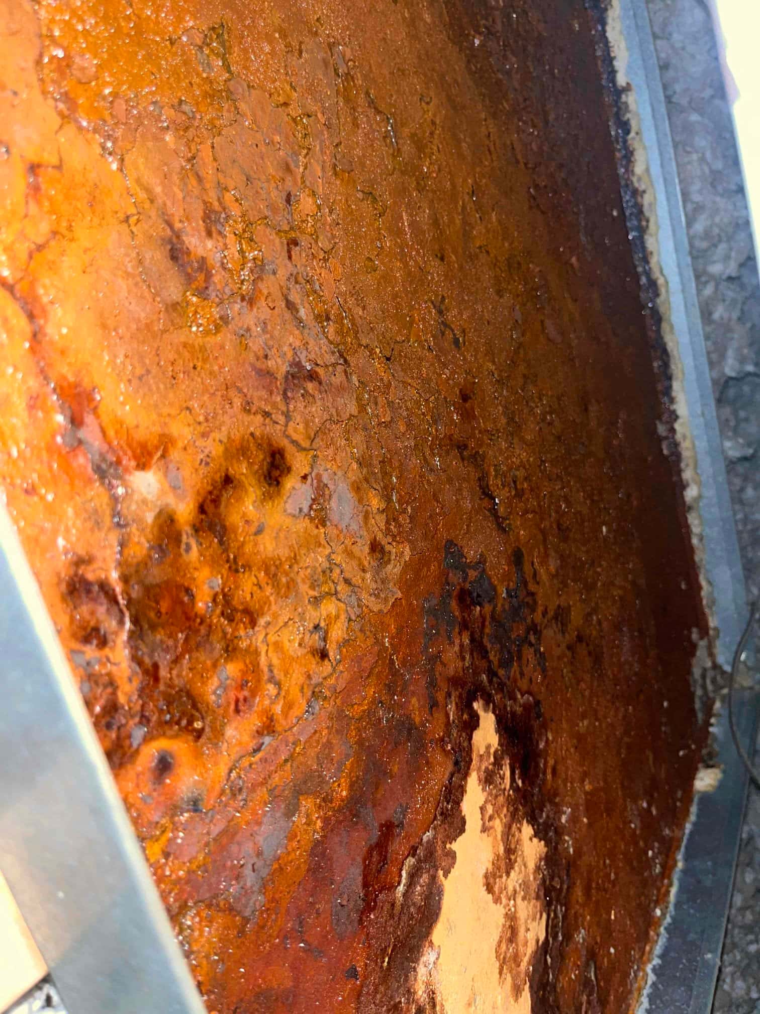 Severely corroded condensate drain pan with heavy rust scale and pitting along the metal surface and edges.