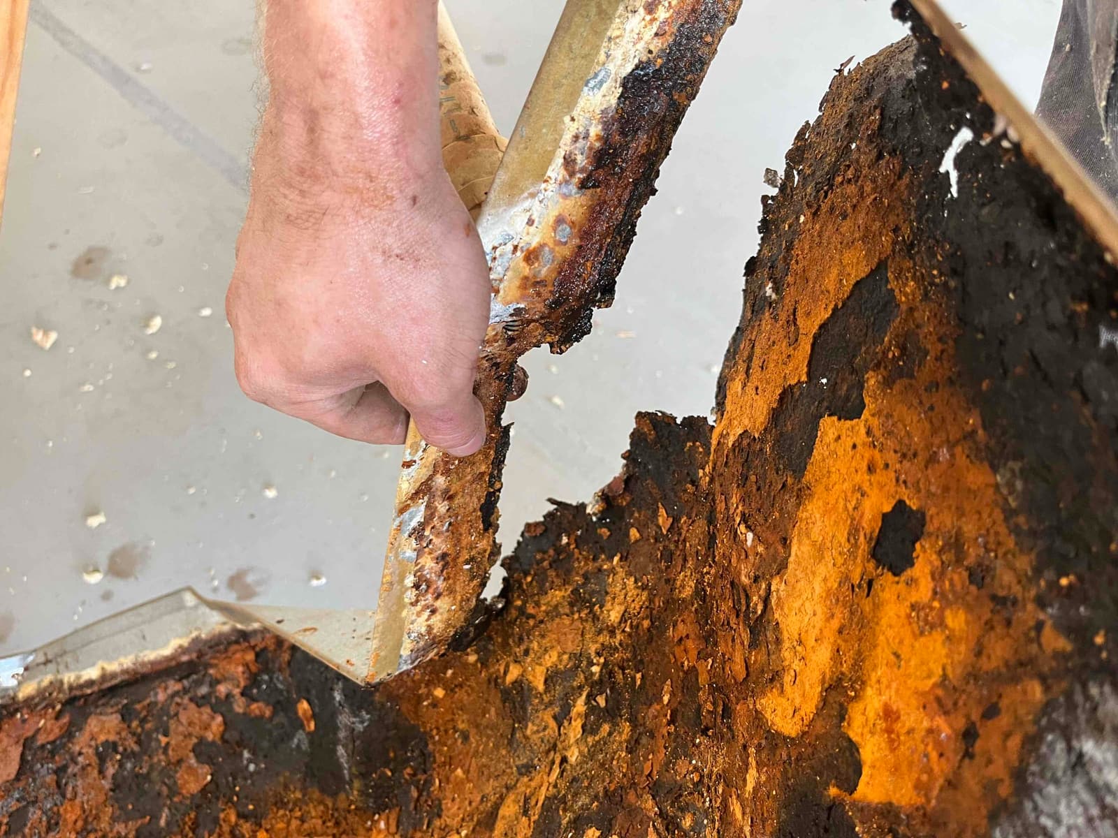 Severely rusted and corroded condensate drain pan removed, showing extensive metal degradation and flaking along the edges.